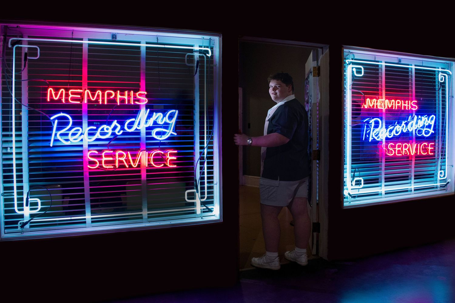 Colorful neon signs illuminate a dark storefront with text including 'Memphis' and 'Service' in bright blue and red lighting.