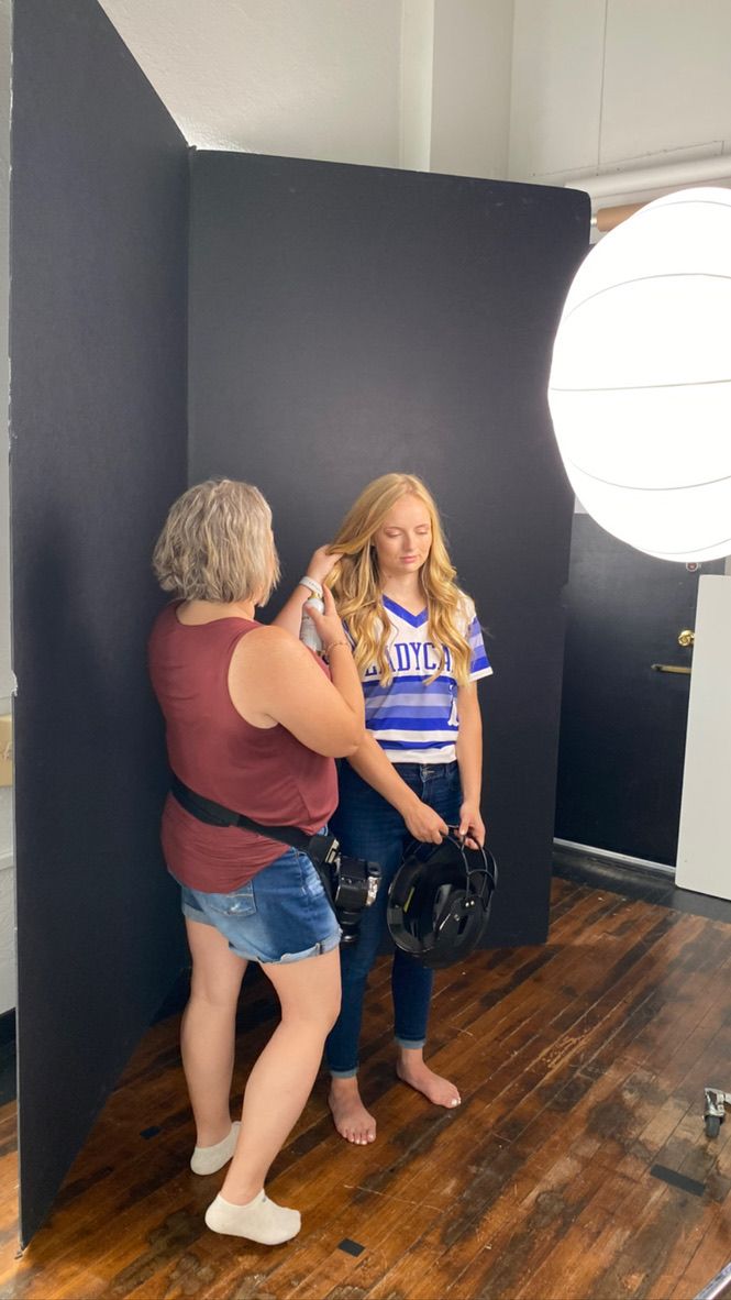 Behind-the-scenes photo shoot in a studio with black backdrop, lighting equipment and wooden floors.