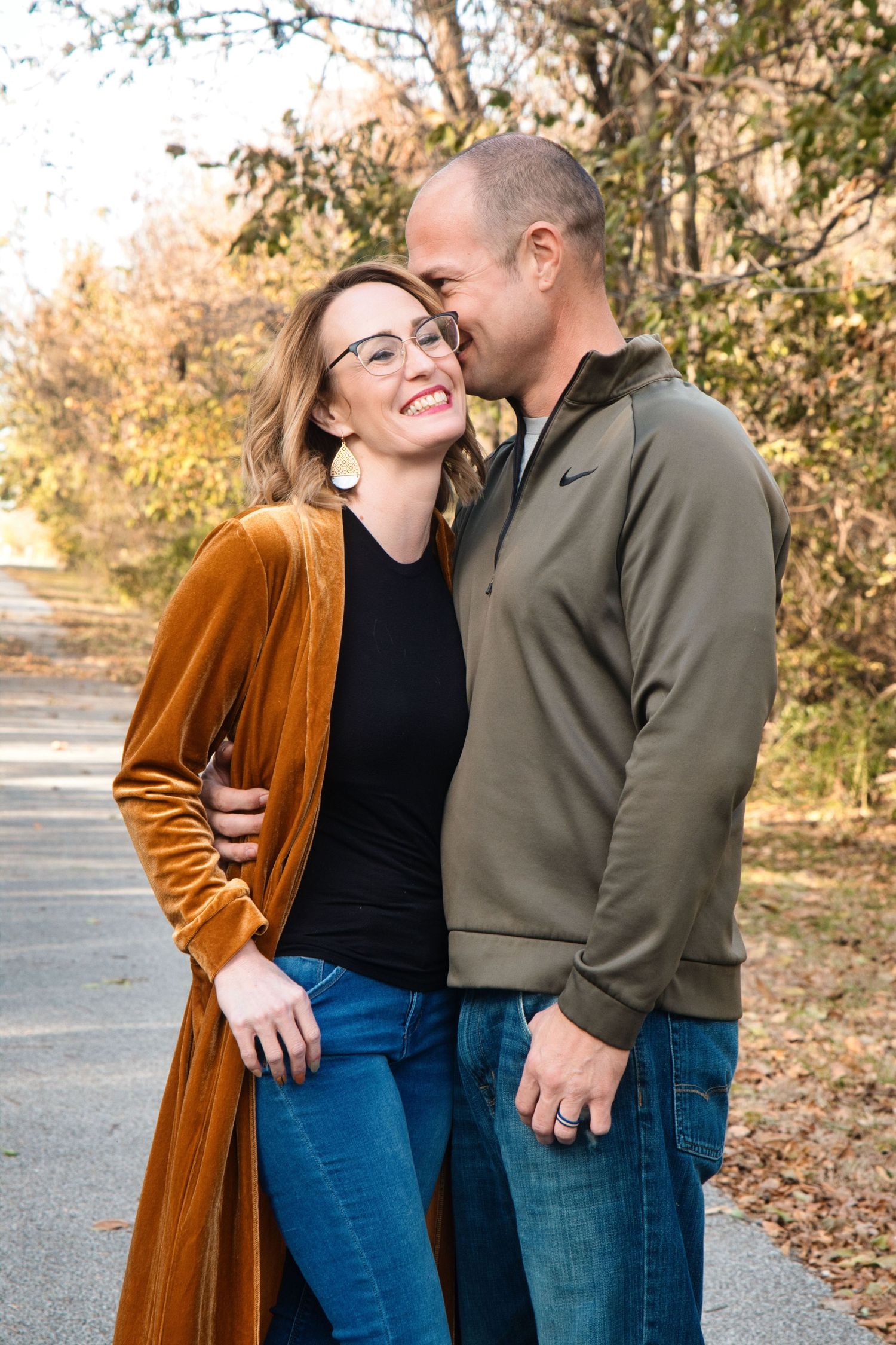 Couple sharing intimate moments and laughter on an autumn path surrounded by trees.