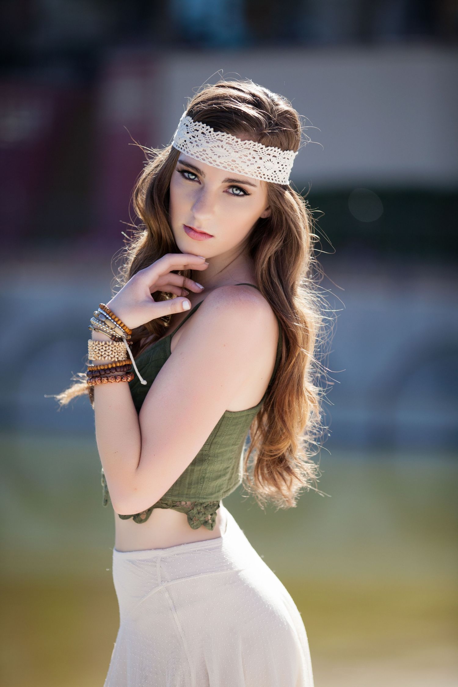 Fashion model in olive green top and white skirt poses outdoors with vintage style netting headpiece.