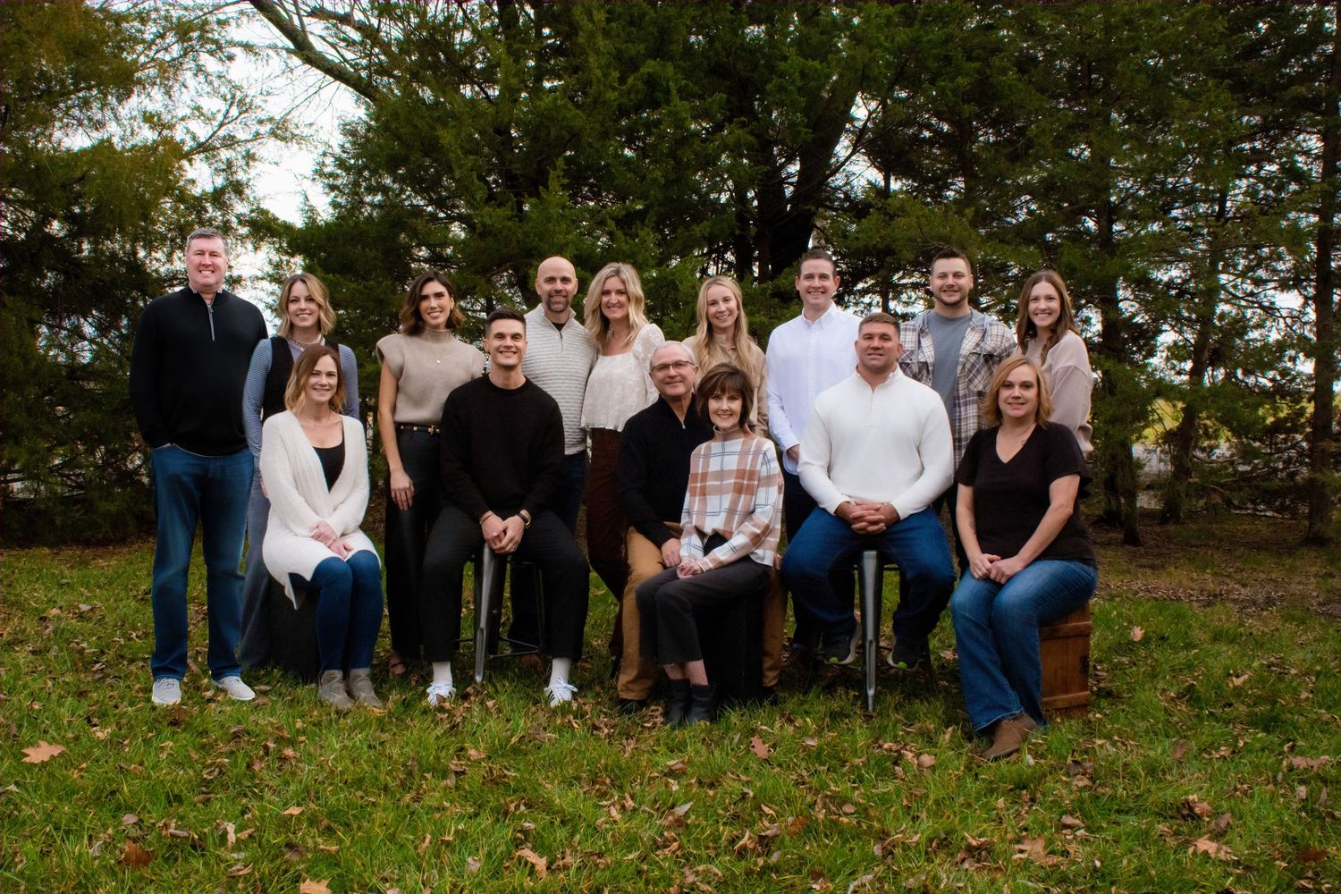 Group photo taken outdoors on a grassy hill with fall foliage and trees in the background.