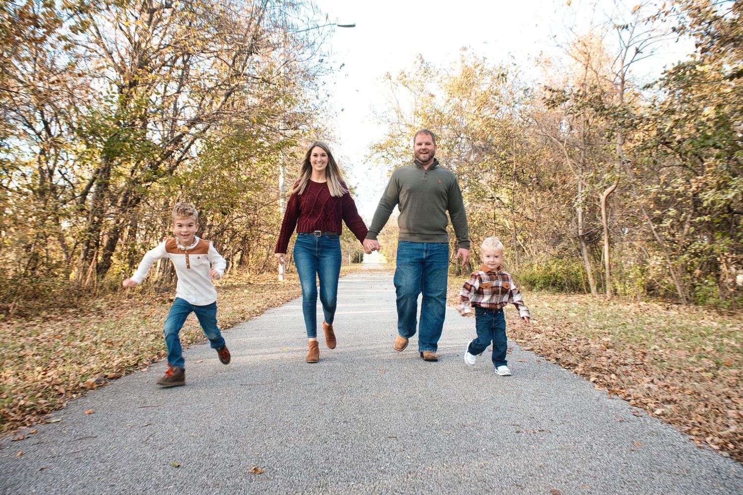 Family members walking and holding hands on a tree-lined path during fall season.