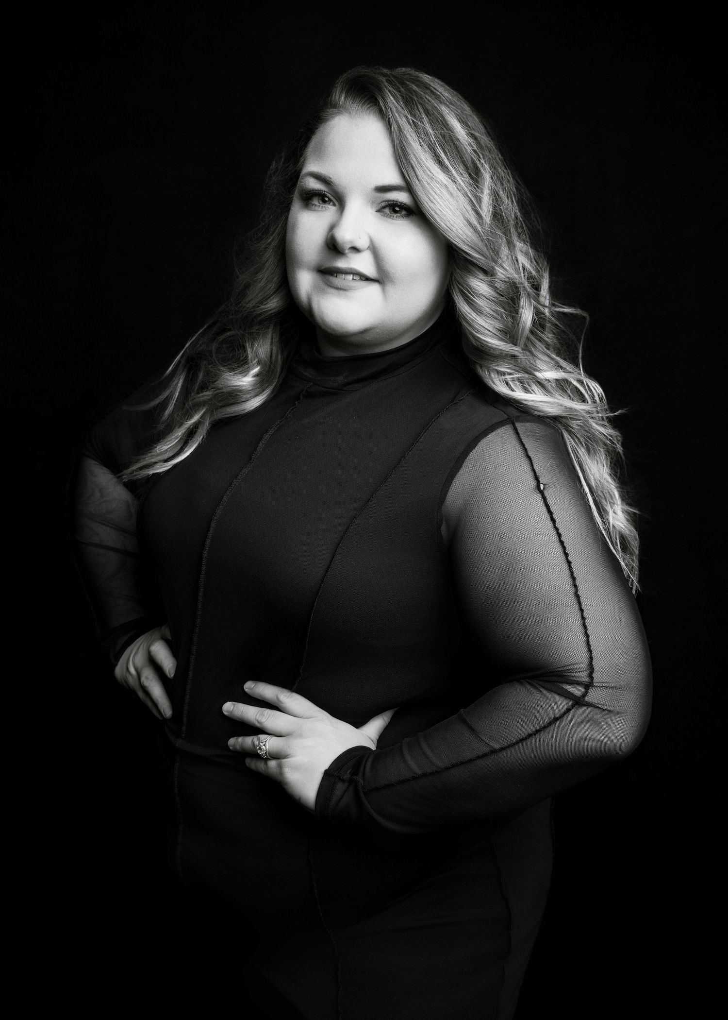 Black and white professional portrait of a woman in a turtleneck top with arms crossed against dark background.