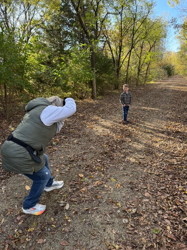 People walking and crouching on a leaf-covered forest trail during autumn.