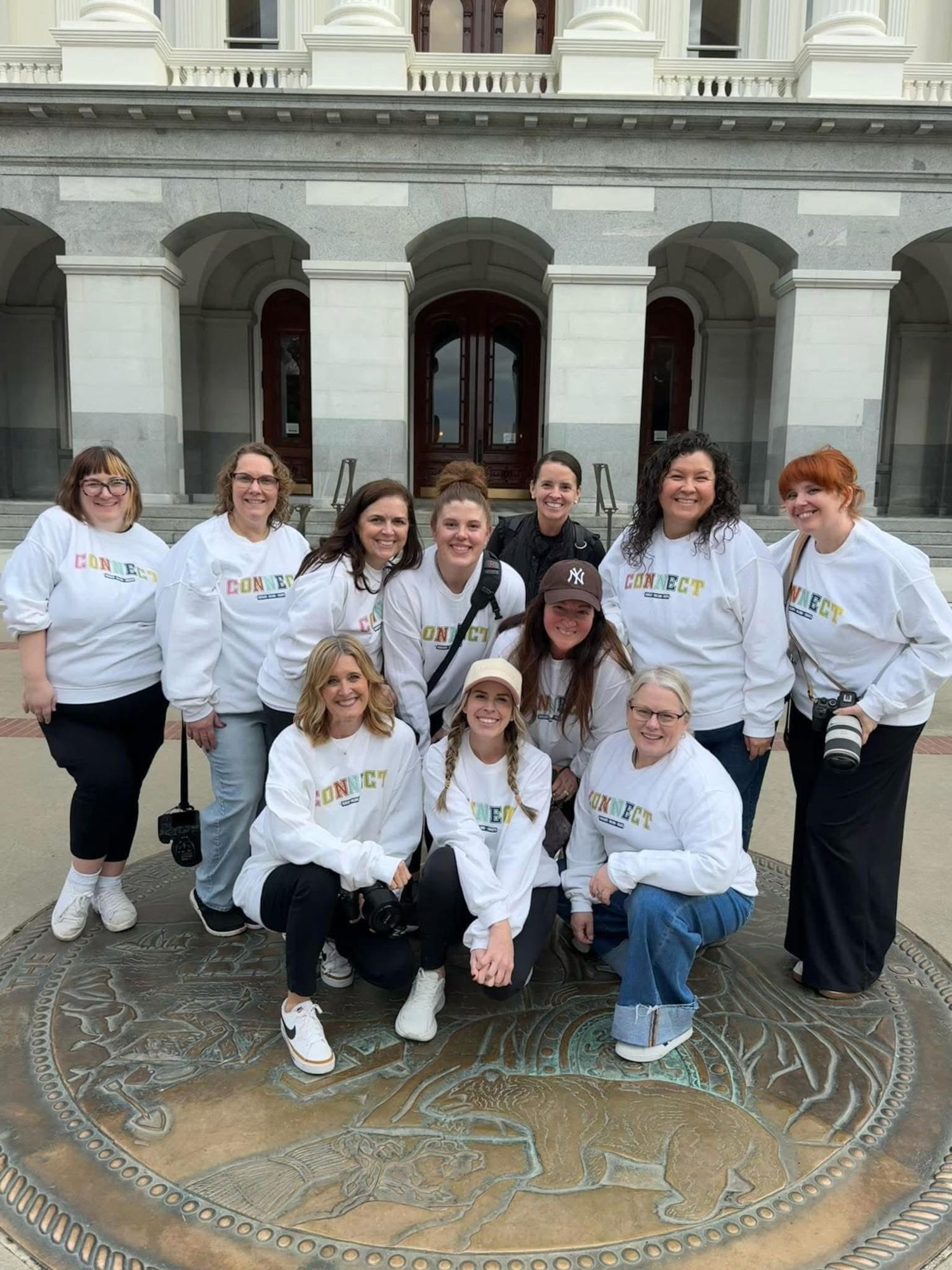 A group wearing matching white shirts poses together in front of a decorative floor design at a historic building.