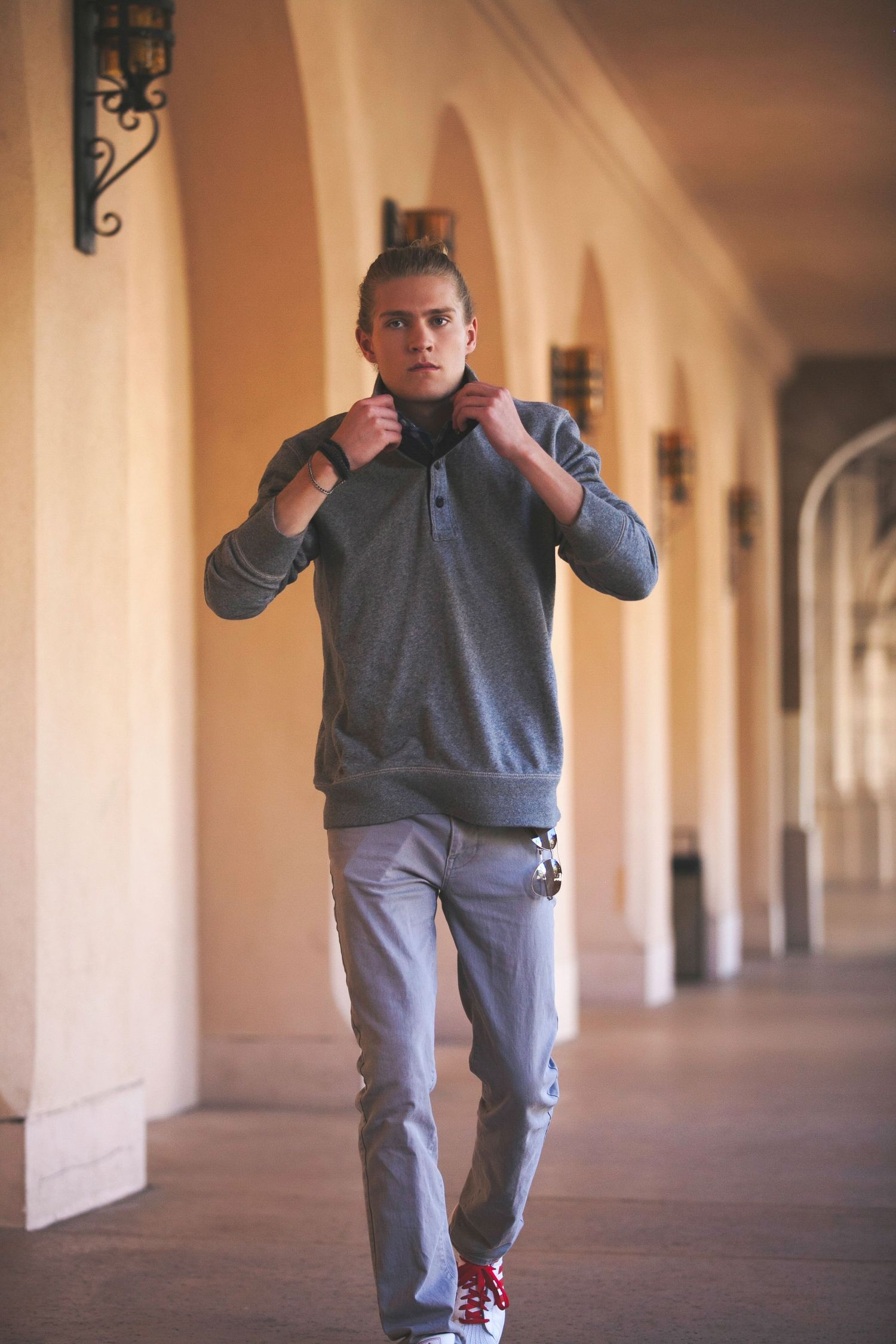 Person in grey sweatsuit performs dynamic dance moves in an elegant hallway with arched columns and warm lighting.