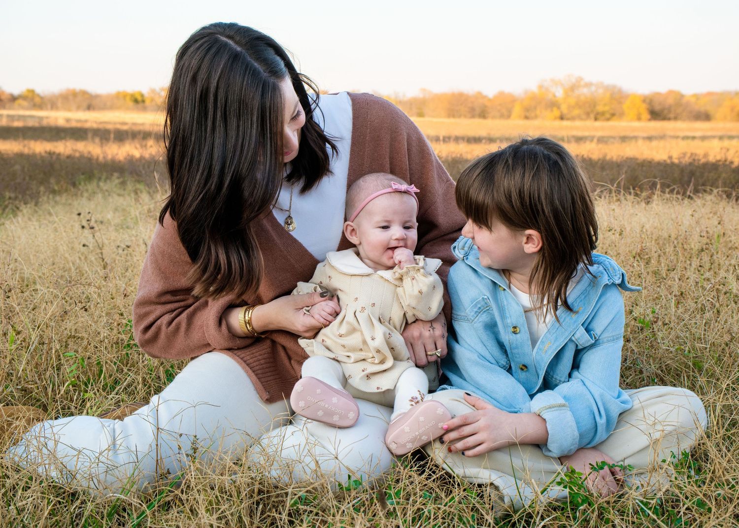 Family lying together on blanket in autumn field during sunset photoshoot.