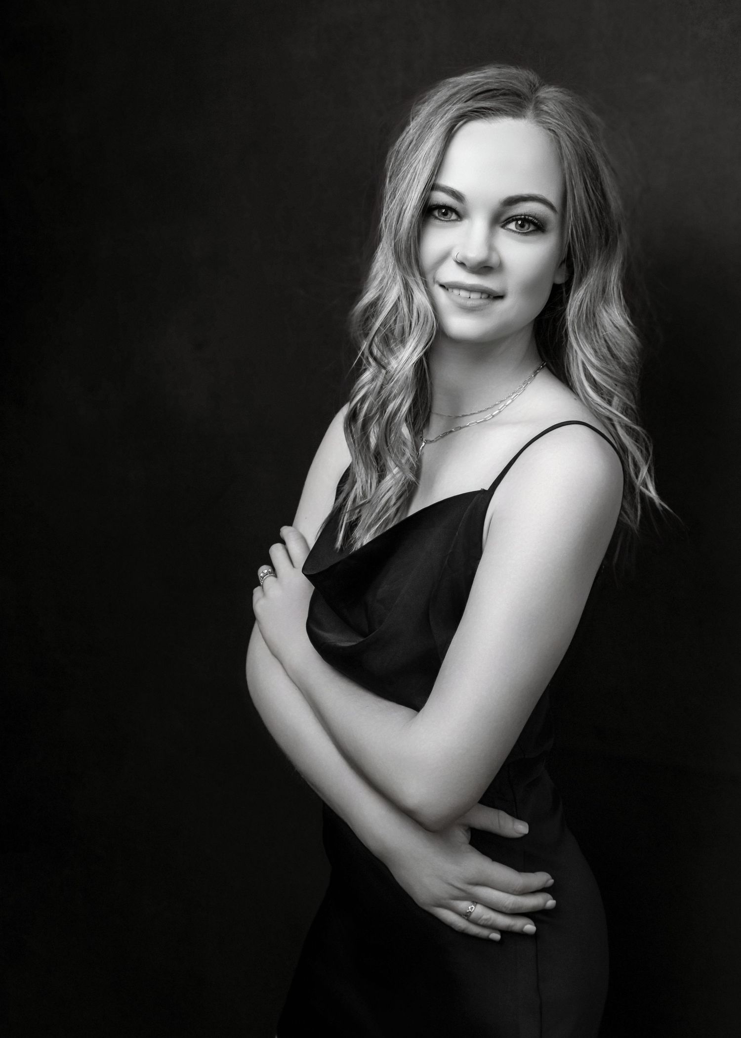 Black and white portrait of a young blonde woman in a black dress, posing elegantly against a dark studio background.