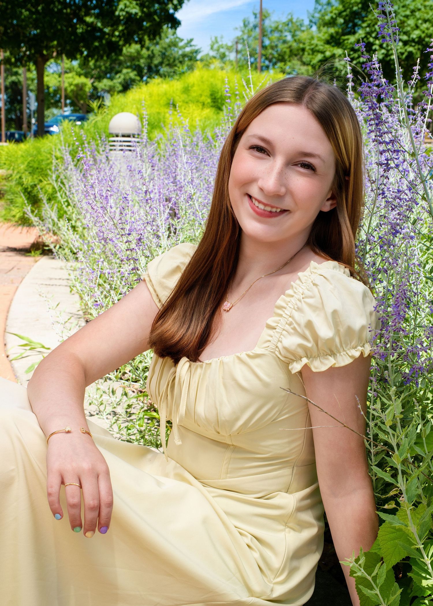 Young woman in yellow dress smiling among purple lavender flowers in a sunny garden.