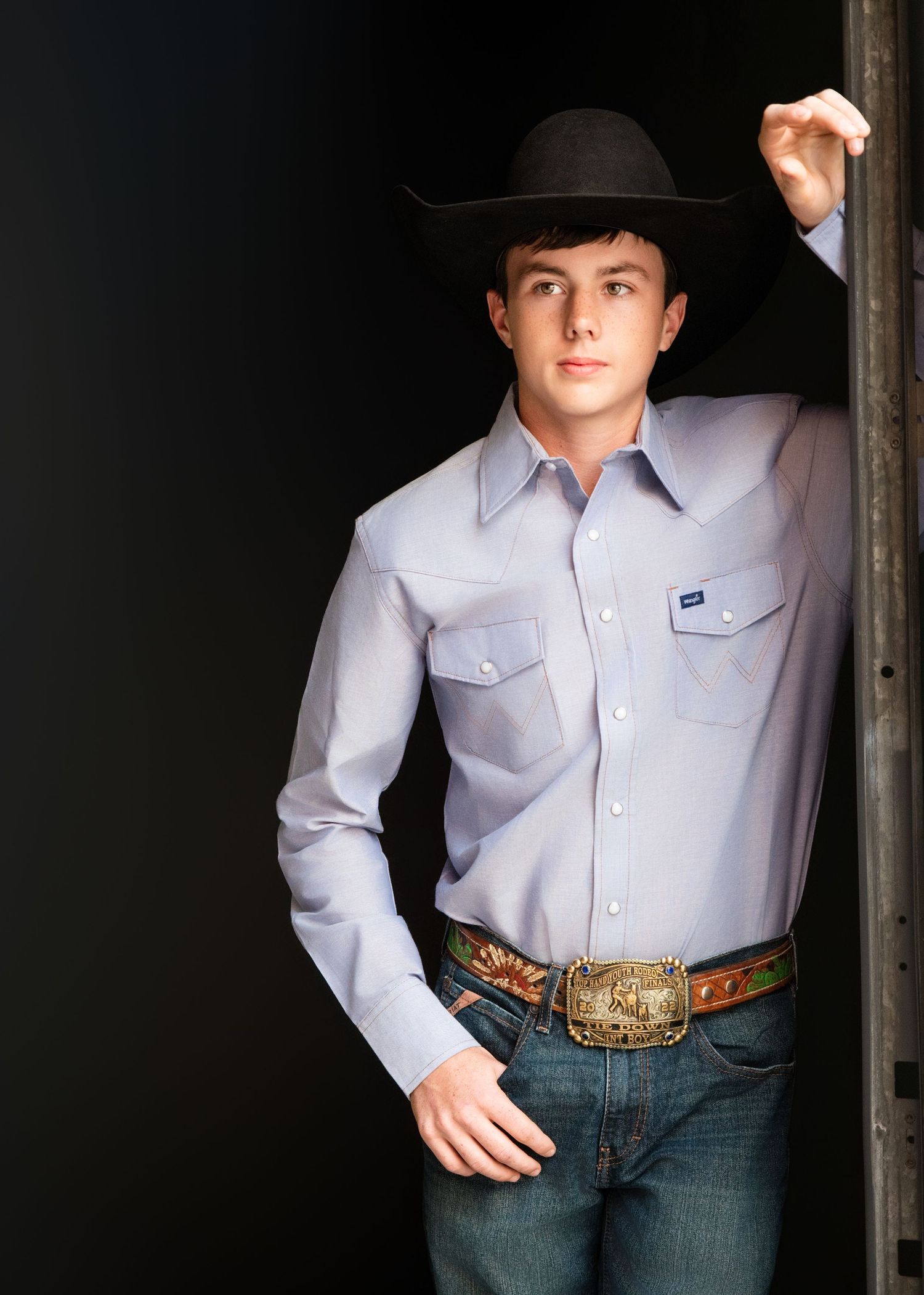 Western style portrait featuring a black cowboy hat, light button-down shirt and decorative belt buckle.