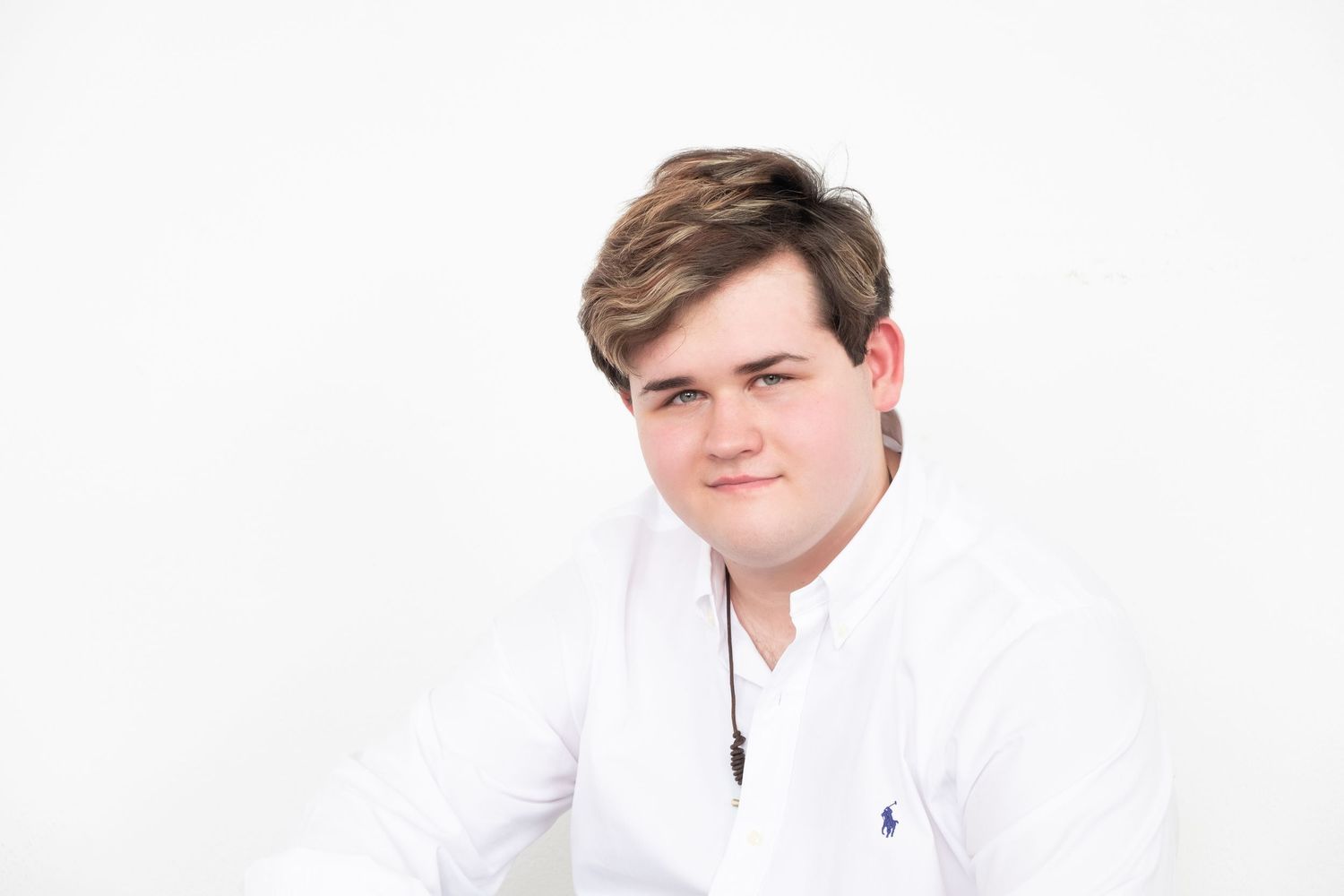 Young man in white Ralph Lauren shirt posing against white background for professional portrait photo.