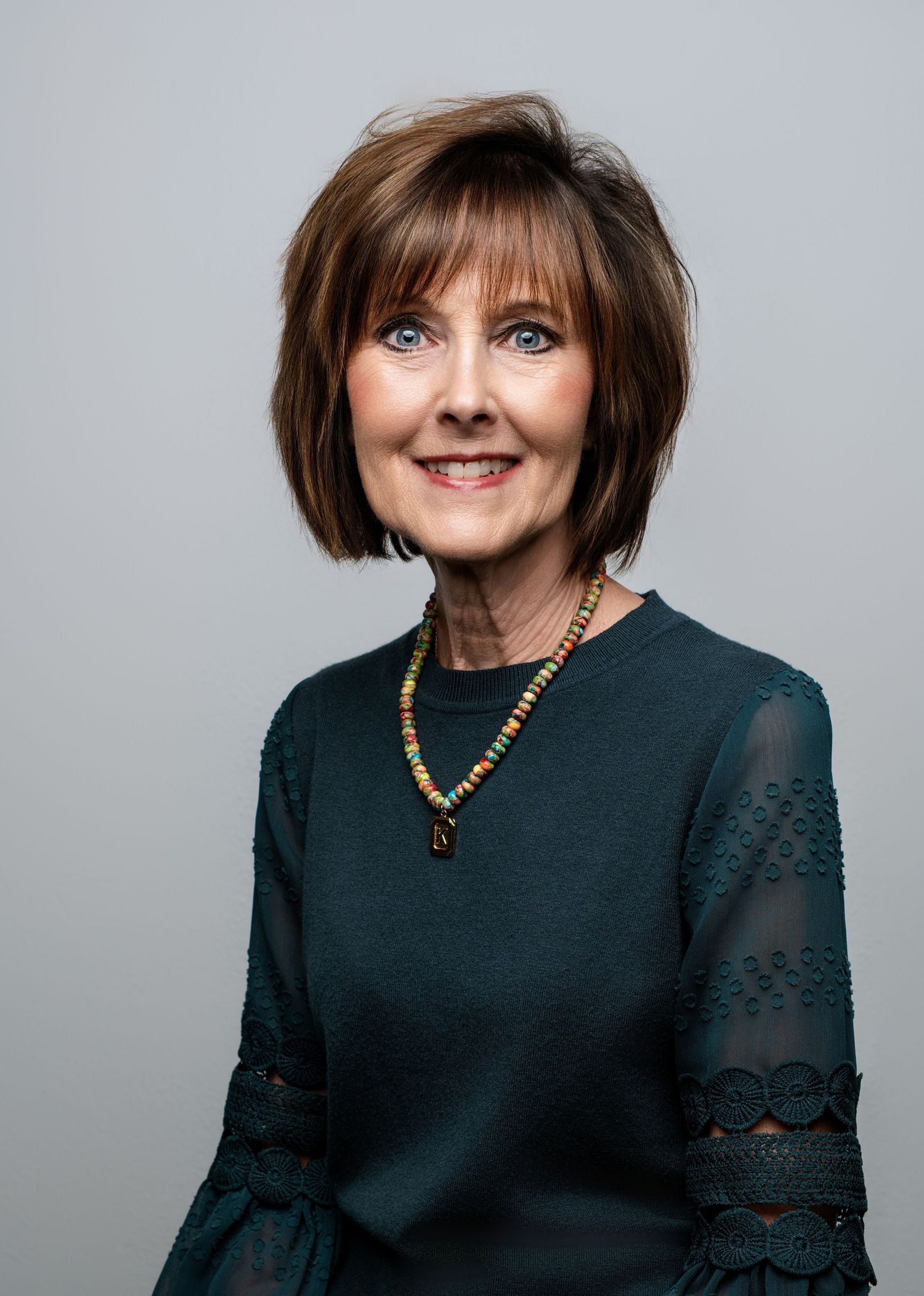 Studio portraits showing someone in a black top with lace sleeves and wooden necklace.