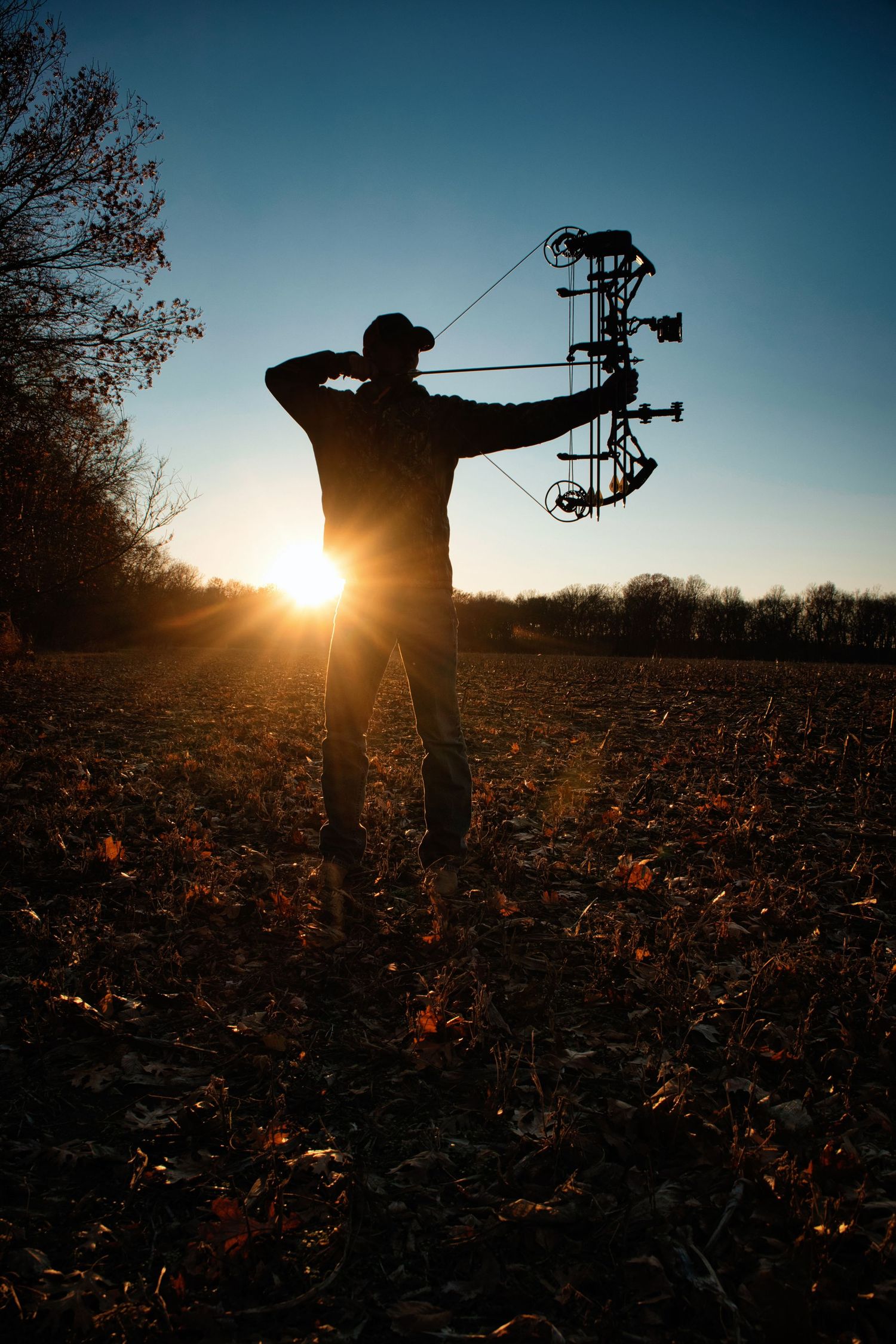 Silhouette of archer drawing compound bow at sunset in field.