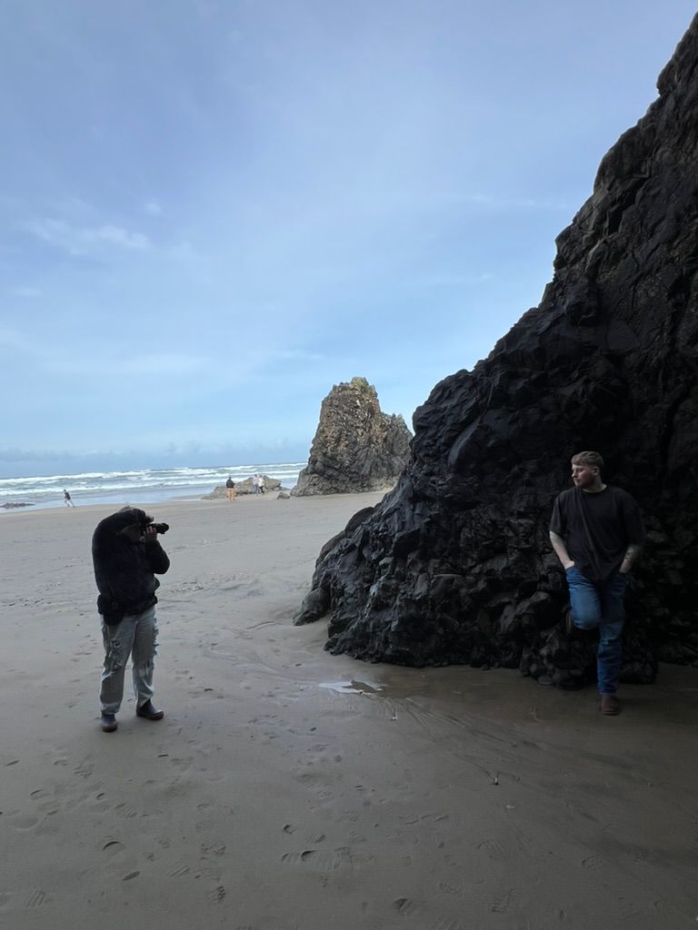 People exploring and taking photos among dramatic black rock formations on a misty coastal beach.