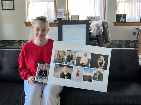 A person wearing a red sweatshirt holds up photo prints while sitting on a dark couch with pictures displayed on the wall.