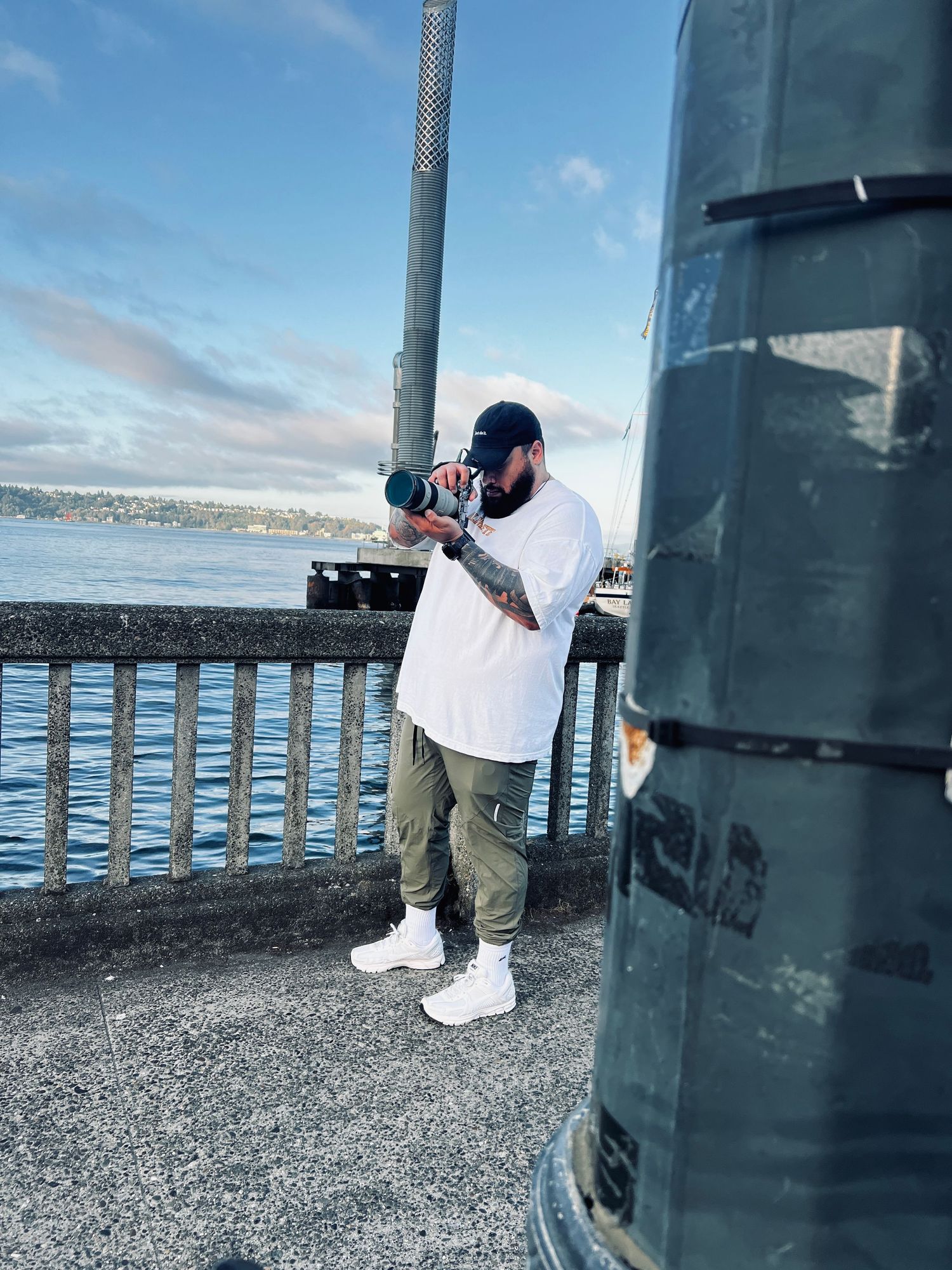 Person in white clothing crouching near a railing against a scenic waterfront backdrop.