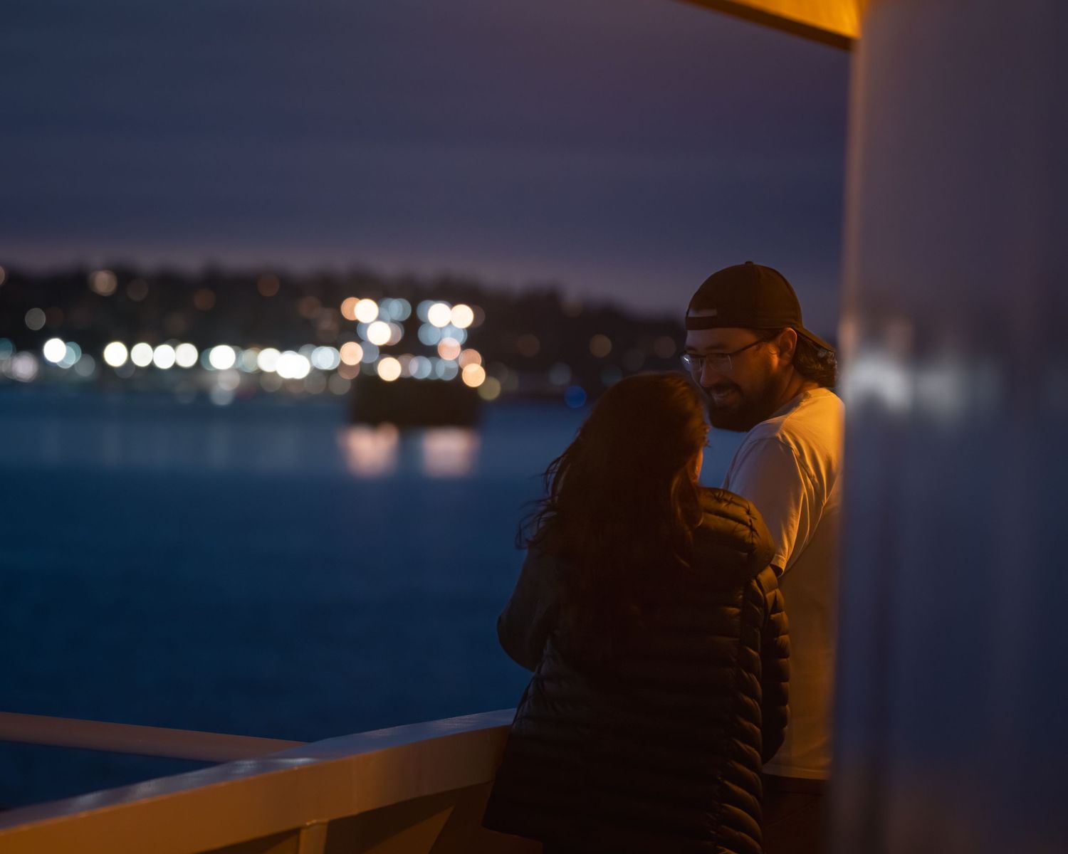 Silhouetted figures against city lights reflecting on dark water during evening hours.