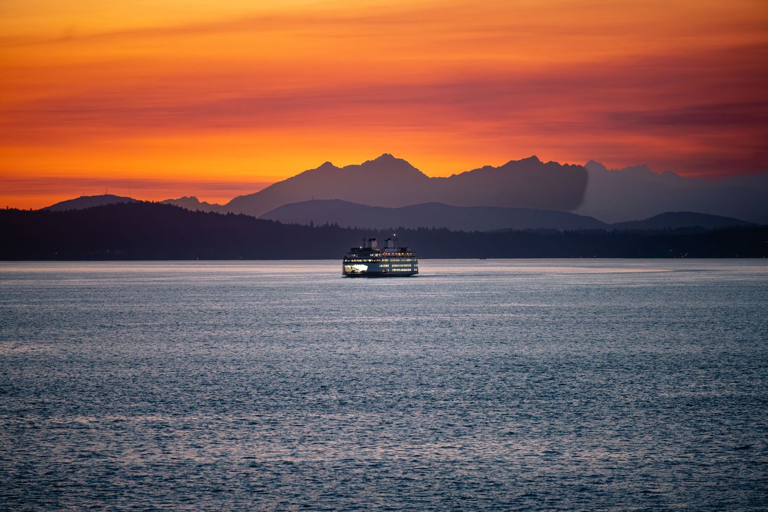 Stunning orange and purple sunset over mountain silhouettes with a boat on calm waters.