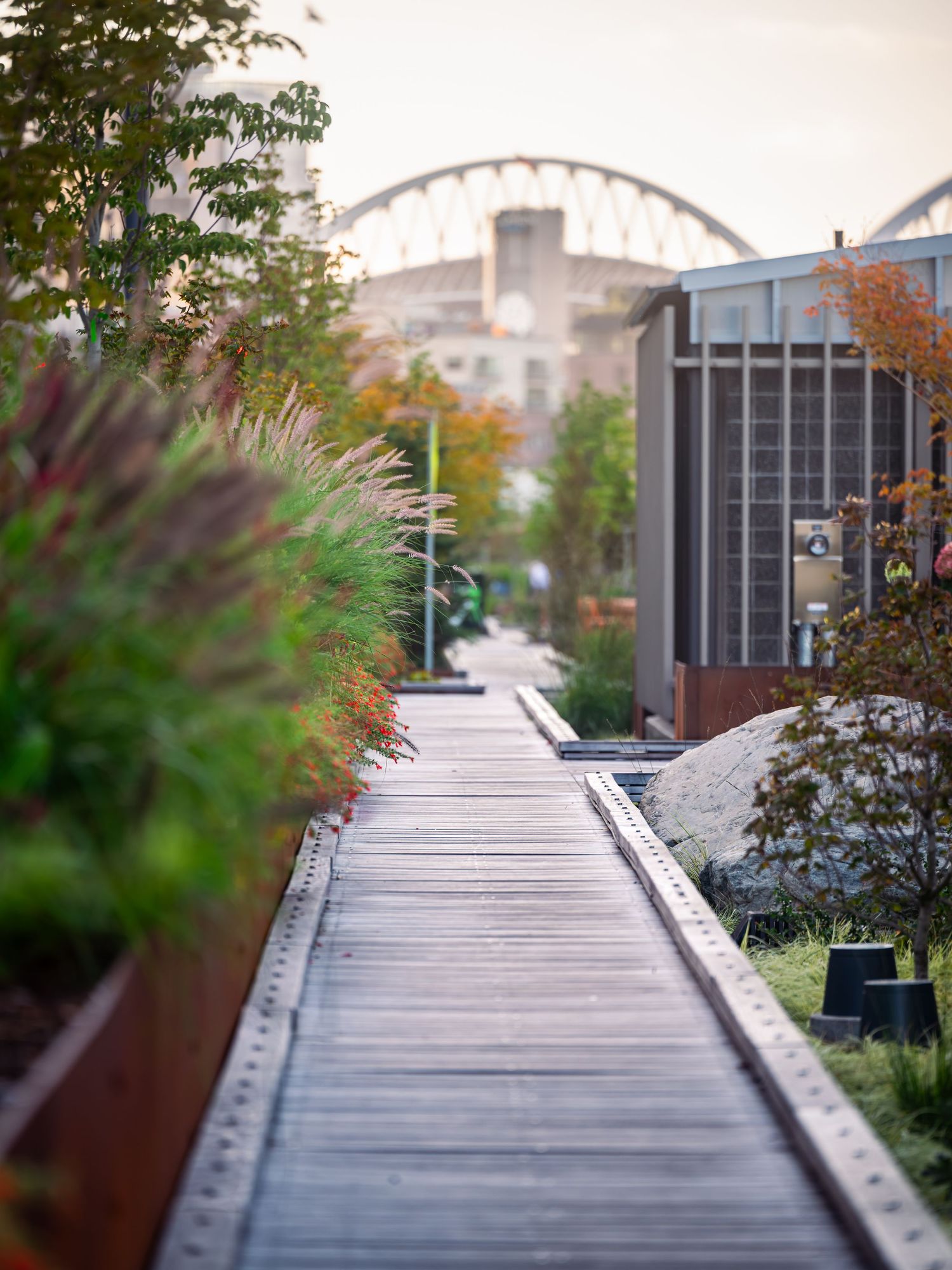 Wooden boardwalk pathway with decorative planters leading to a bridge in the distance.