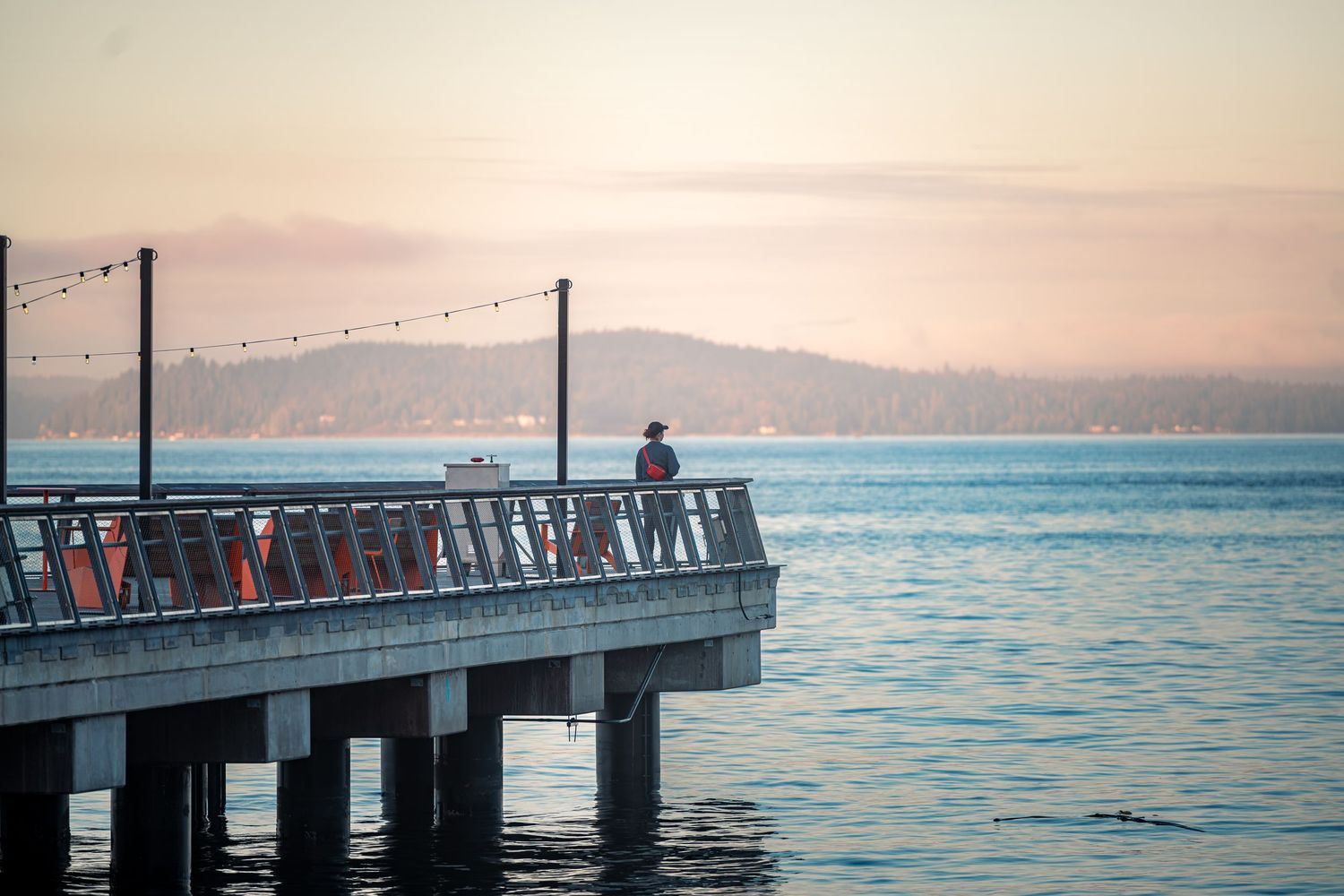 Scenic pier extending into calm waters at sunset with mountains visible in the background.