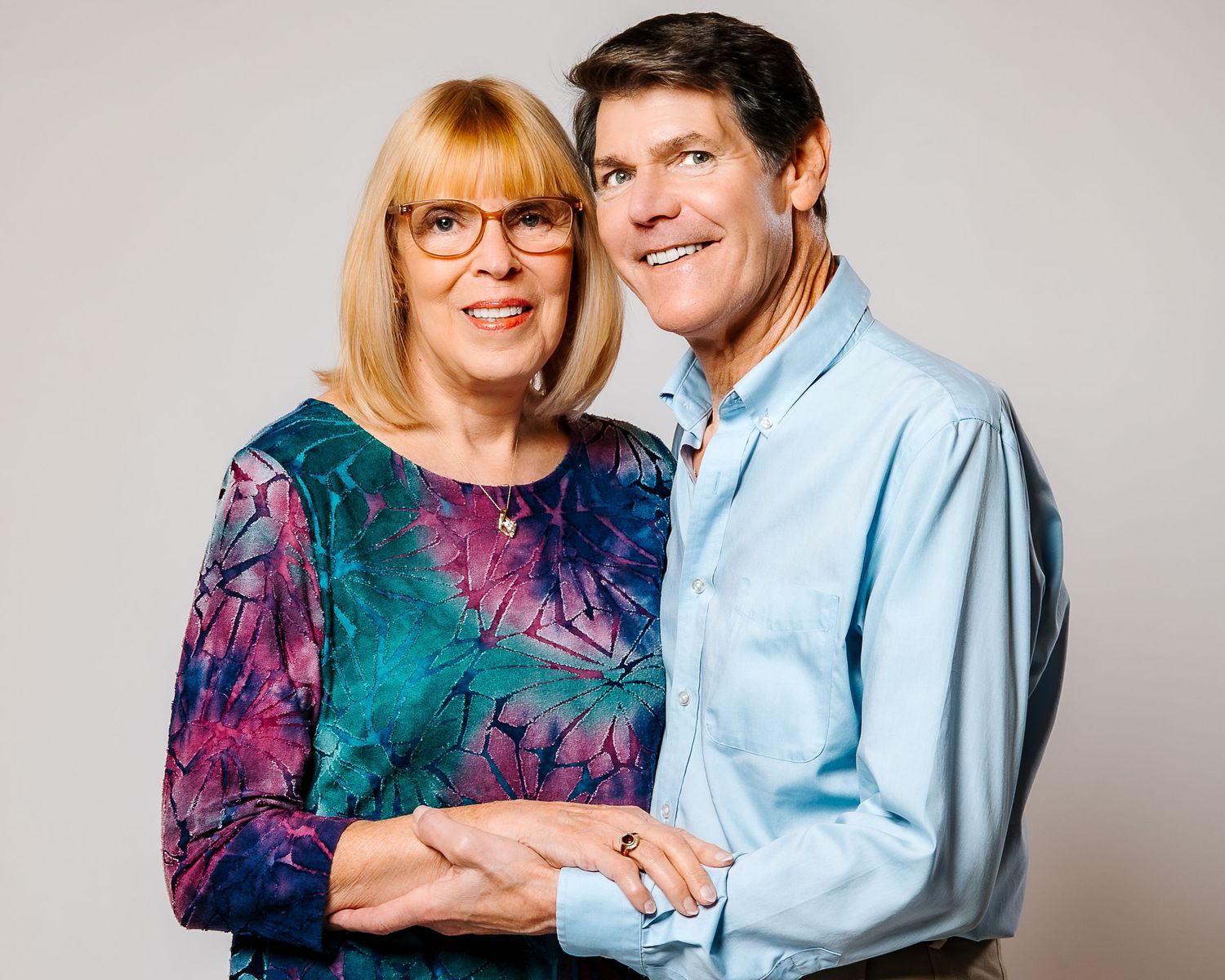 Smiling middle-aged couple posing together affectionately against a neutral studio background.