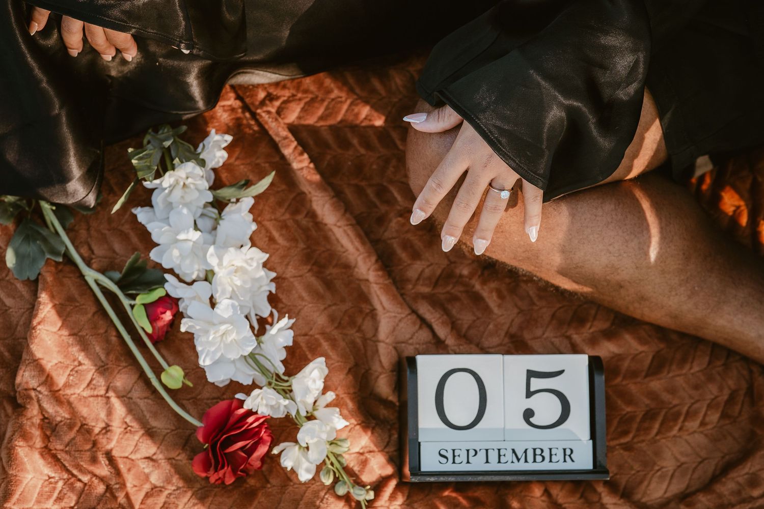 Flat lay of holding hands beside white and red roses and a September 5th date block on a blanket.