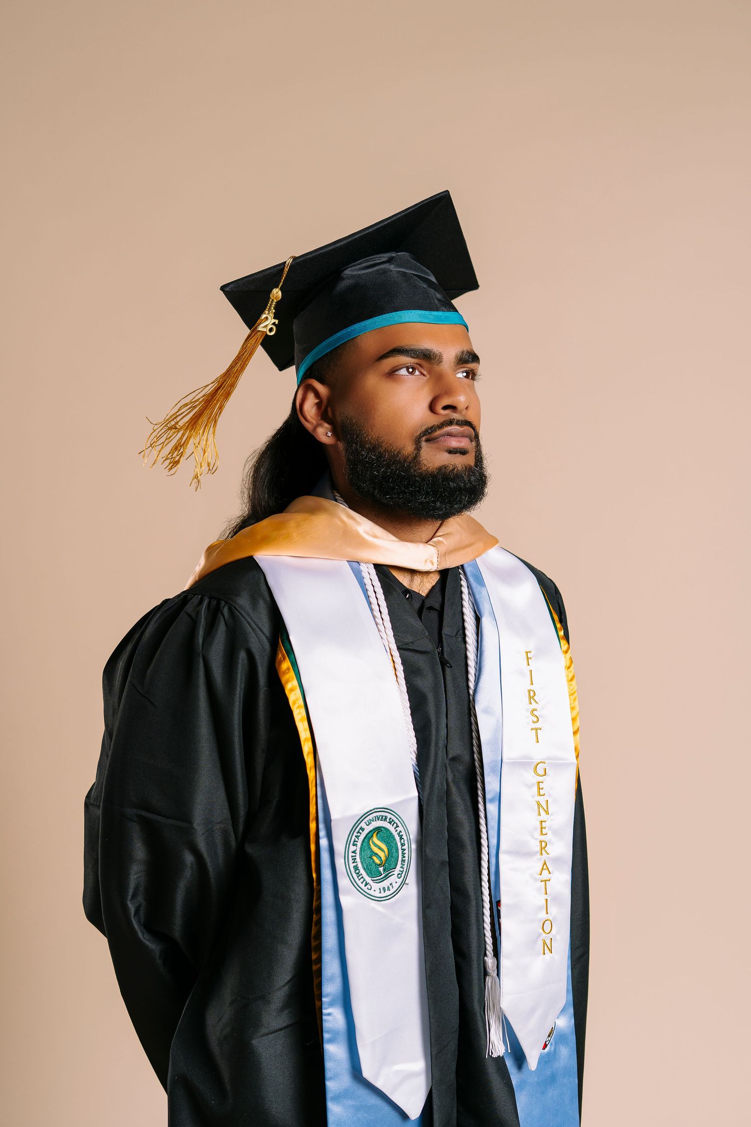 Male graduate in cap and gown with First Generation stole looking up.