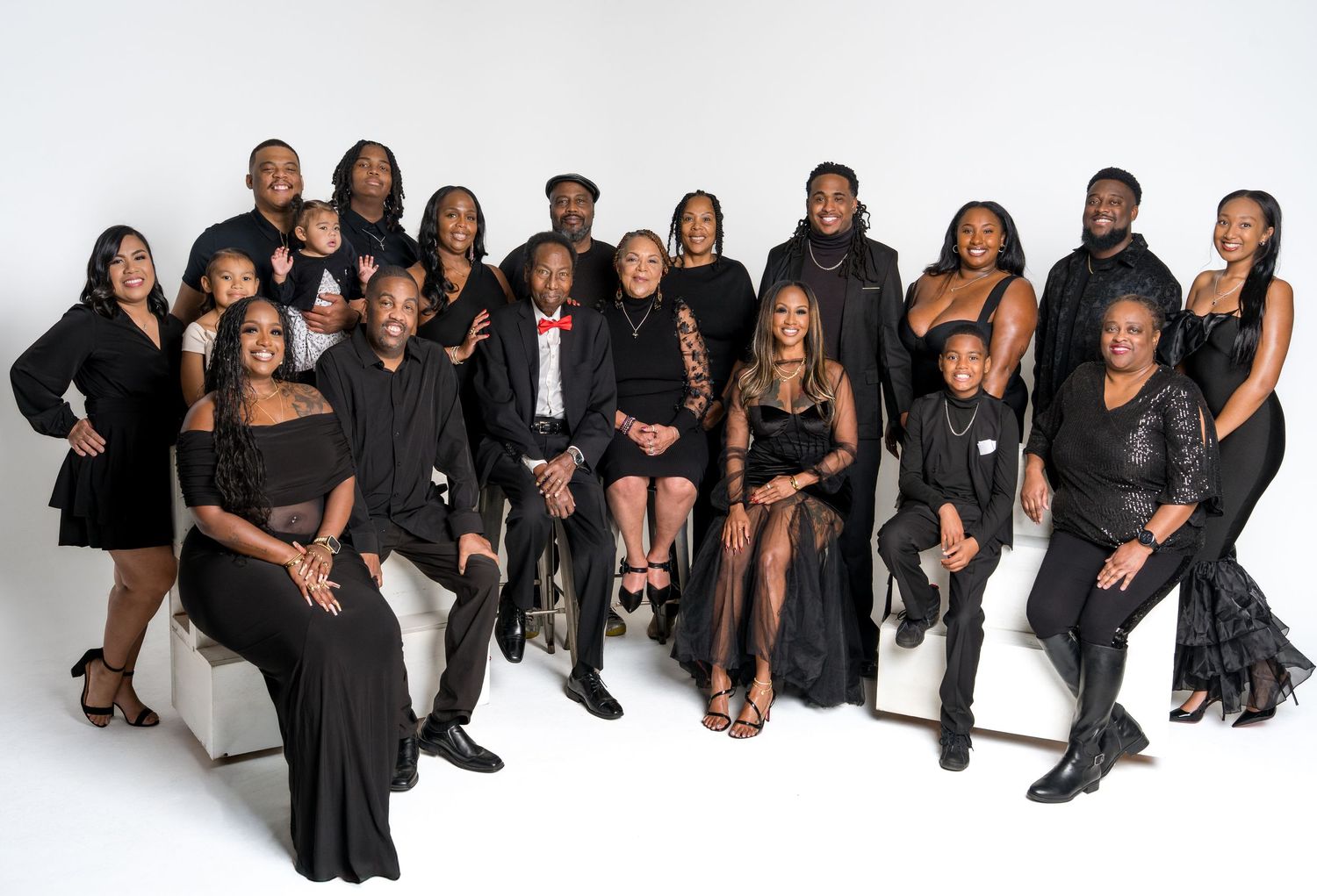 A large extended family group poses together in matching black formal attire for a studio portrait.