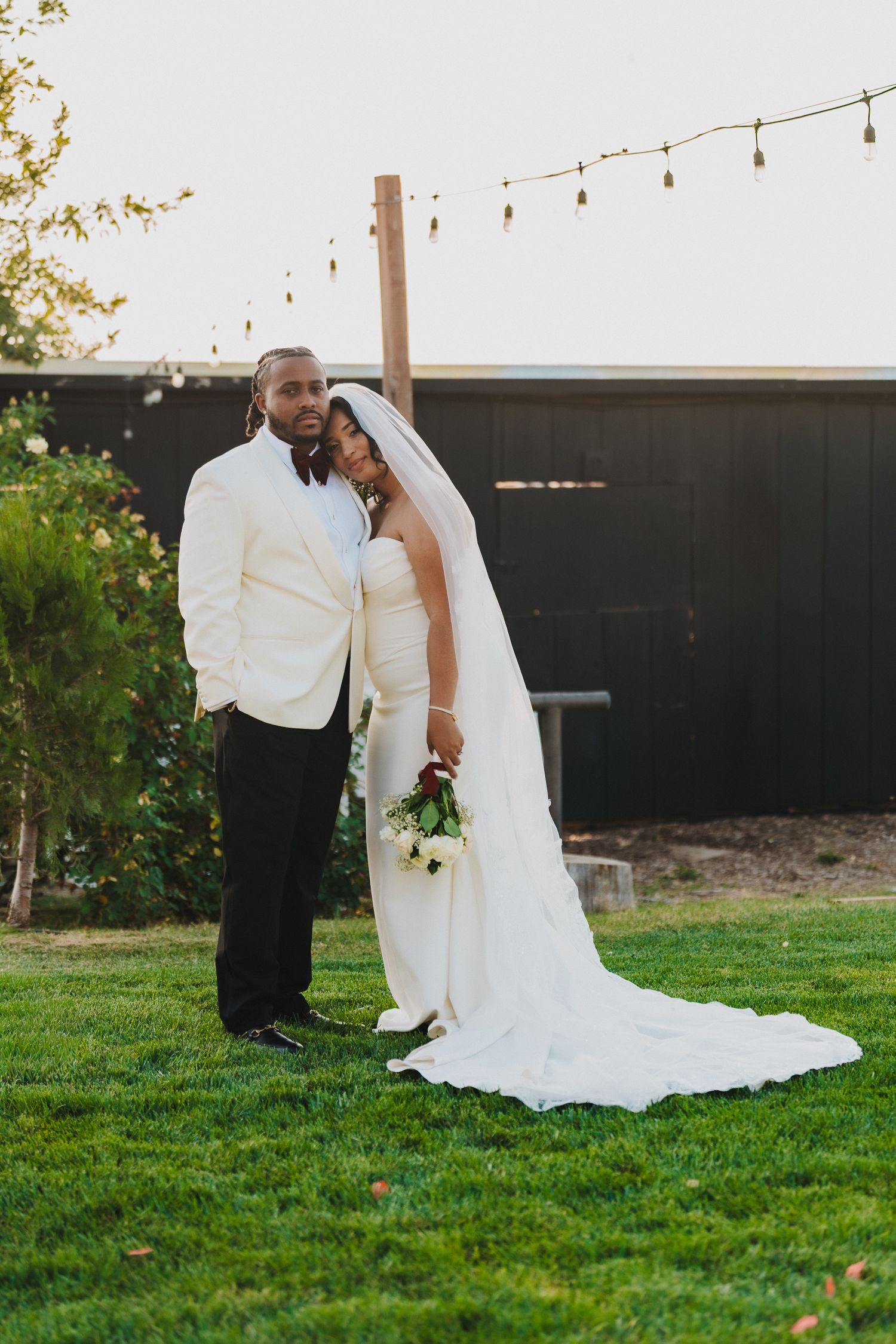 Elegant bride and groom posing together on green grass at golden hour outdoor wedding reception.