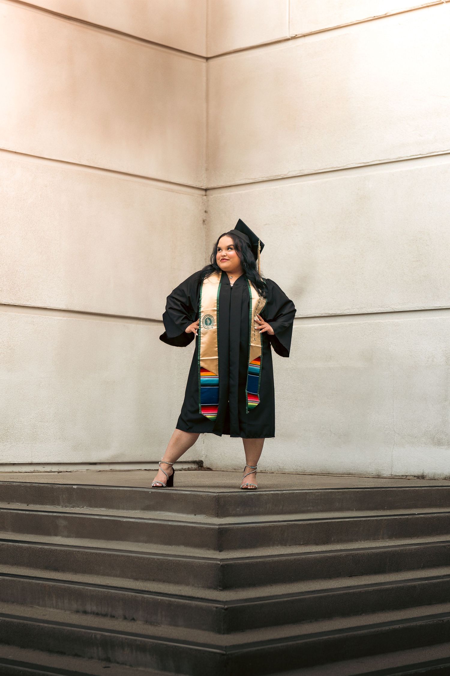 Graduate in cap and gown posing on outdoor steps