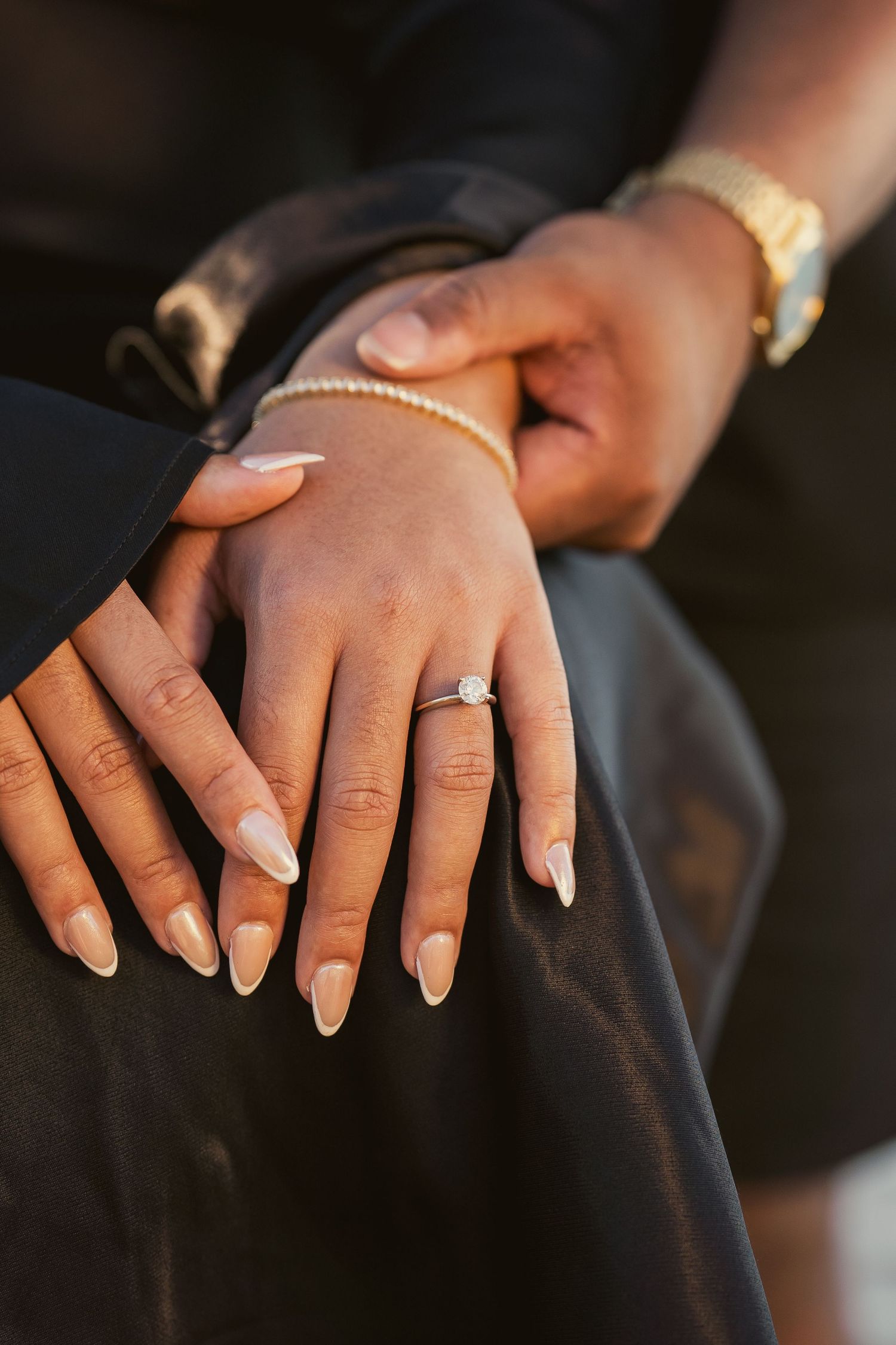 Close-up of bride's hand with diamond engagement ring and pearl bracelet resting on groom's hand.