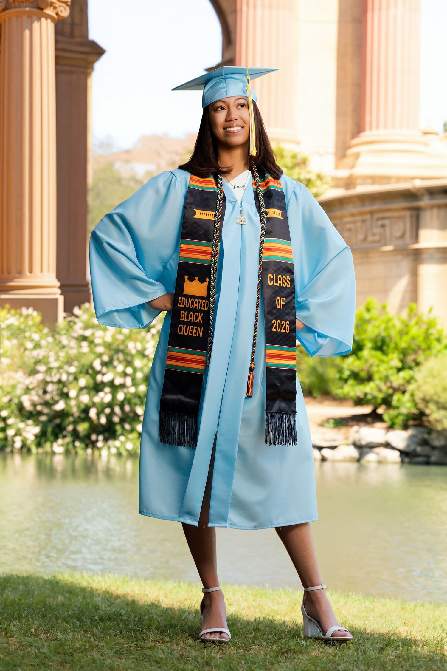 Graduate in light blue cap and gown with Educated Black Queen kente stole, Class of 2025.