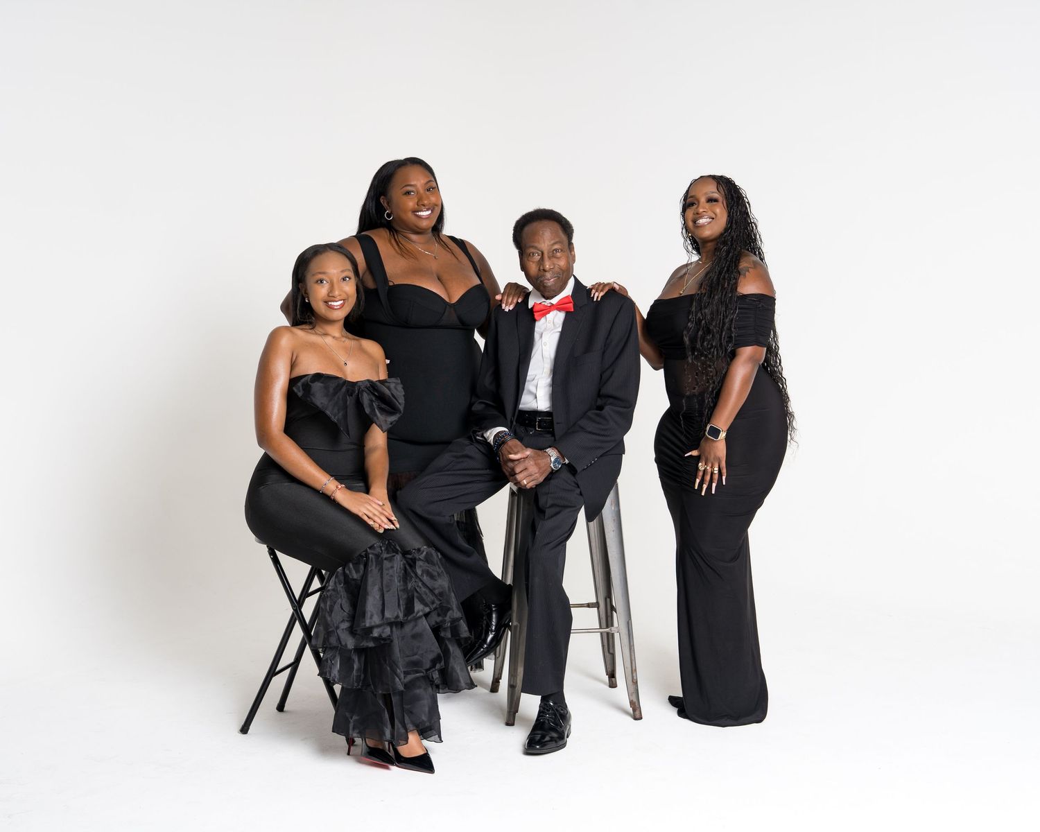 Four people in elegant black formal wear pose together for a professional studio portrait photo.
