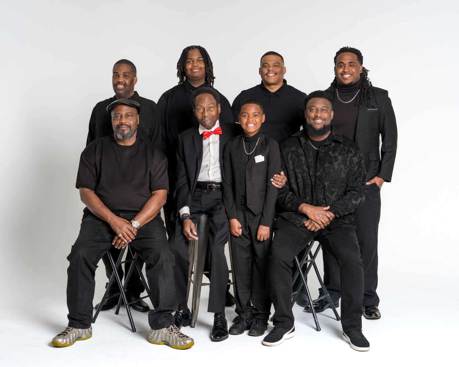 Group of eight men and boys in dark outfits pose for formal family photo.