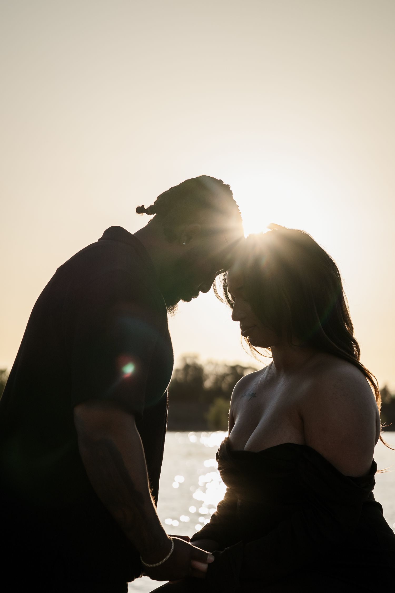 Romantic silhouette of a couple touching foreheads at golden sunset by the water.