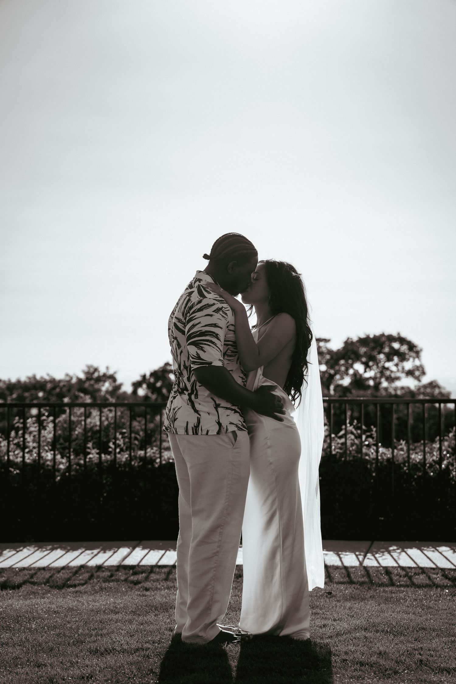Black and white photo of newlyweds sharing a kiss outdoors on their wedding day.