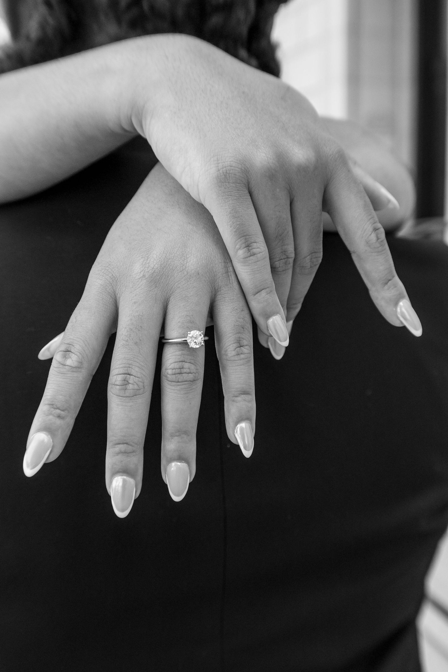 Close-up of a woman's hands displaying a diamond engagement ring with elegant white manicured nails.