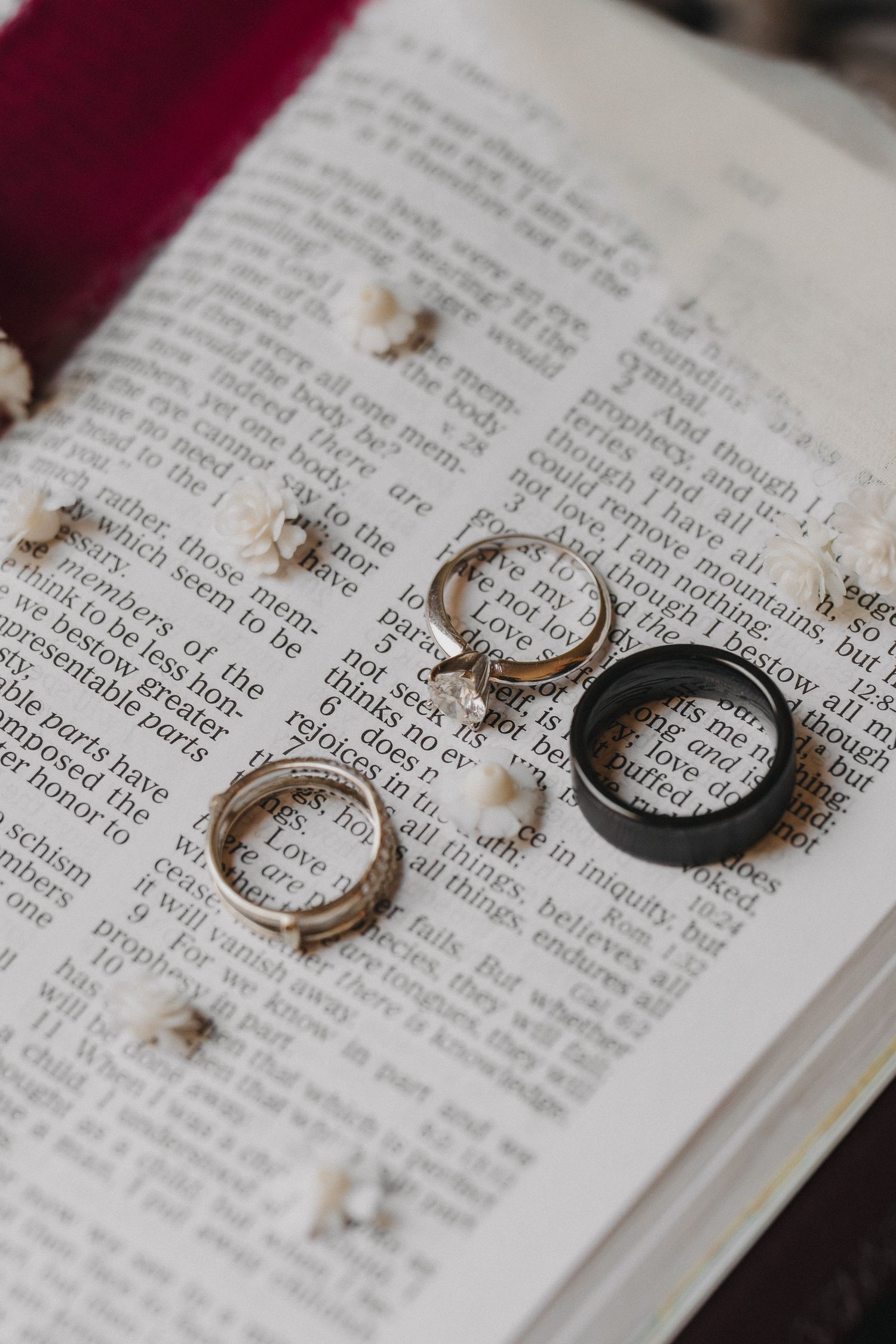 Wedding rings and engagement ring displayed on open Bible with small white flowers.