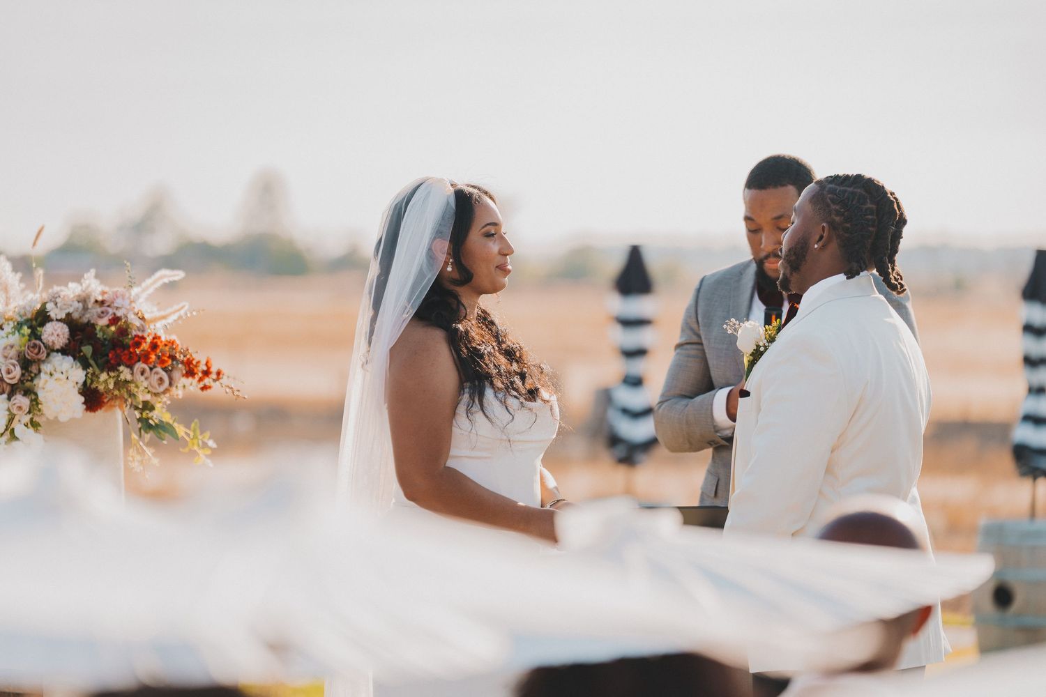 Bride and groom exchanging vows with officiant at outdoor wedding ceremony at golden hour sunset.