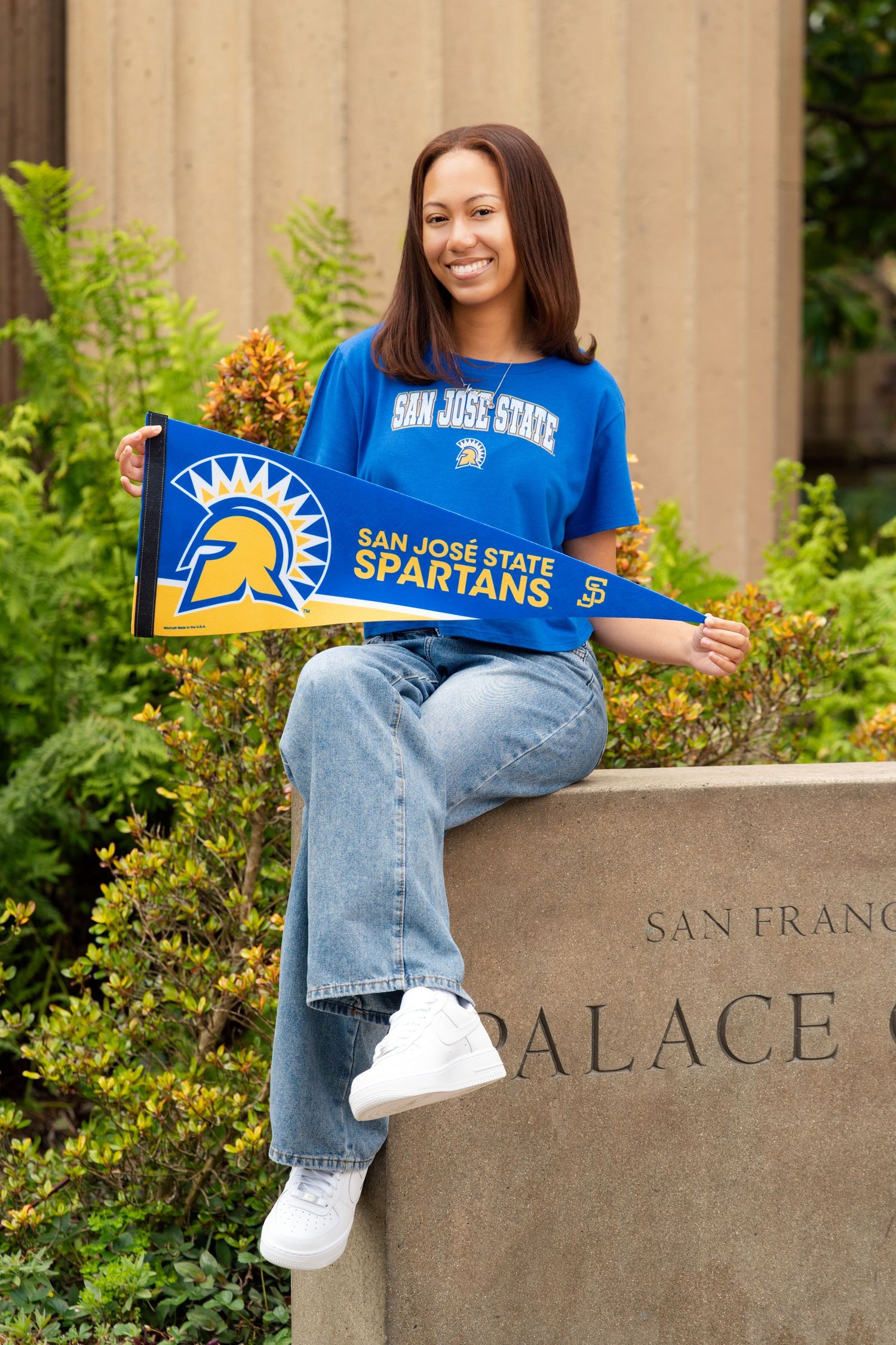 Smiling woman holding San Jose State Spartans pennant sitting on monument at Palace of Fine Arts.