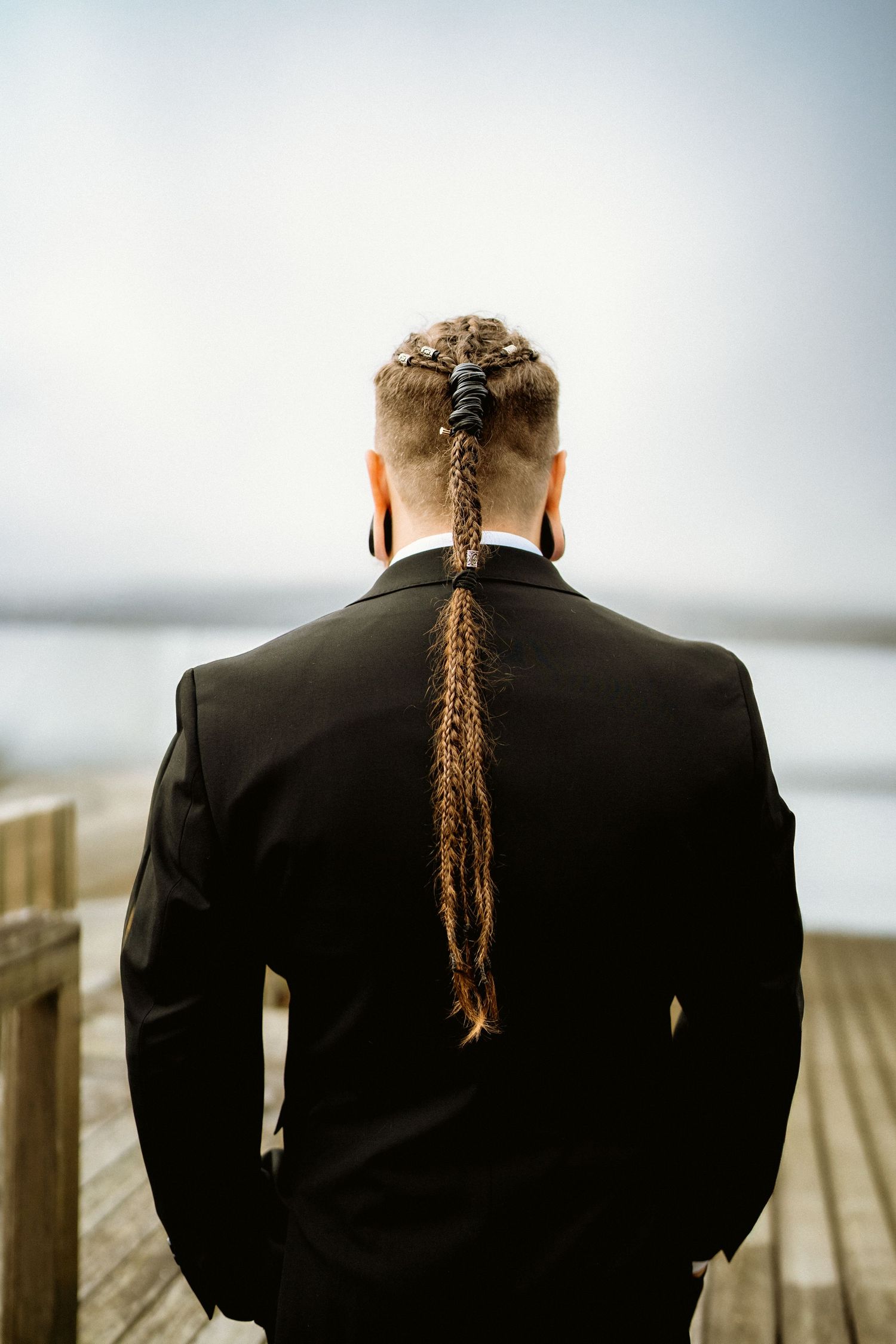 Groom in a black suit photographed from behind near the water