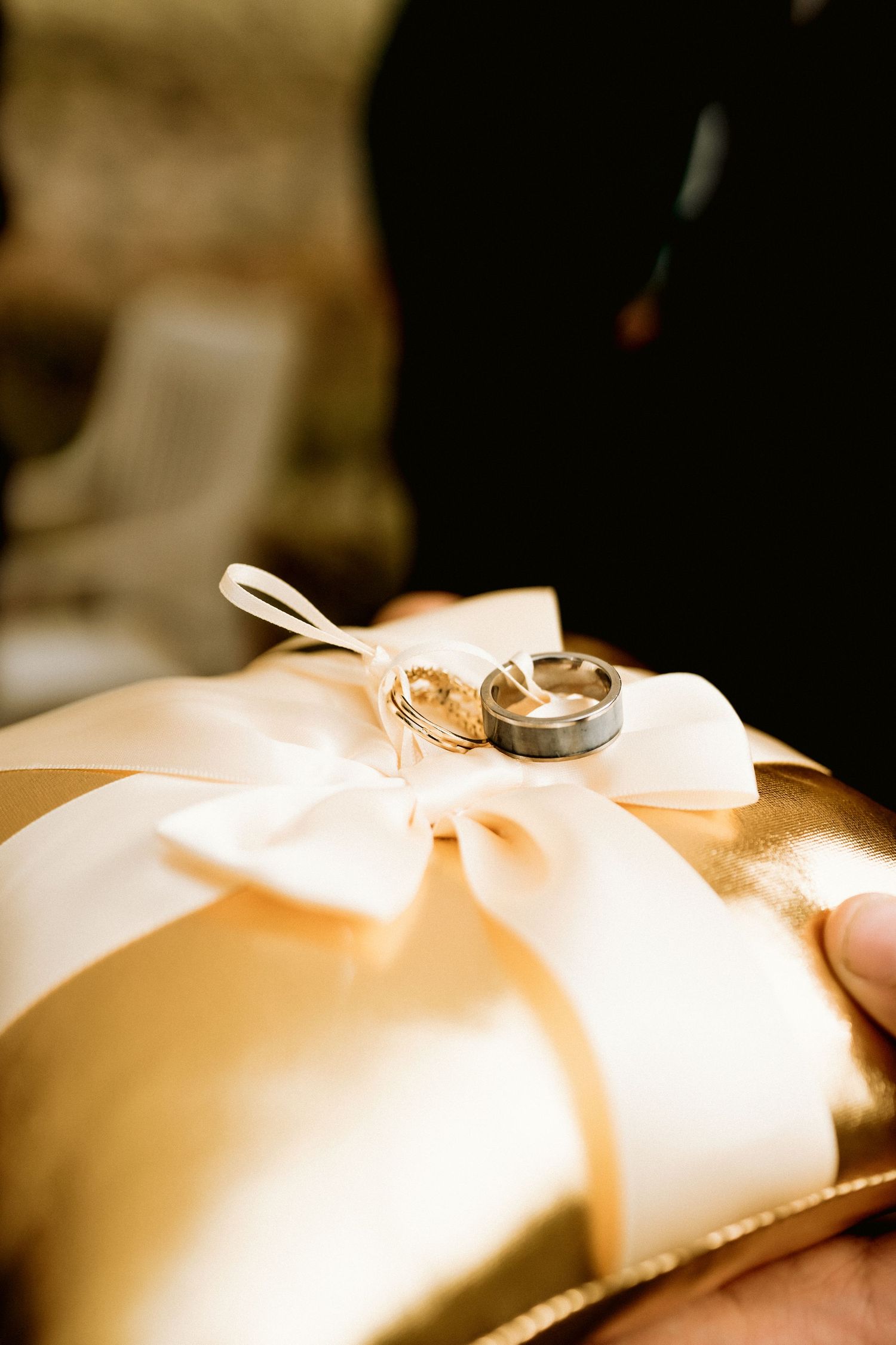 Two gold and silver wedding bands displayed on elegant ivory satin ring bearer pillow.