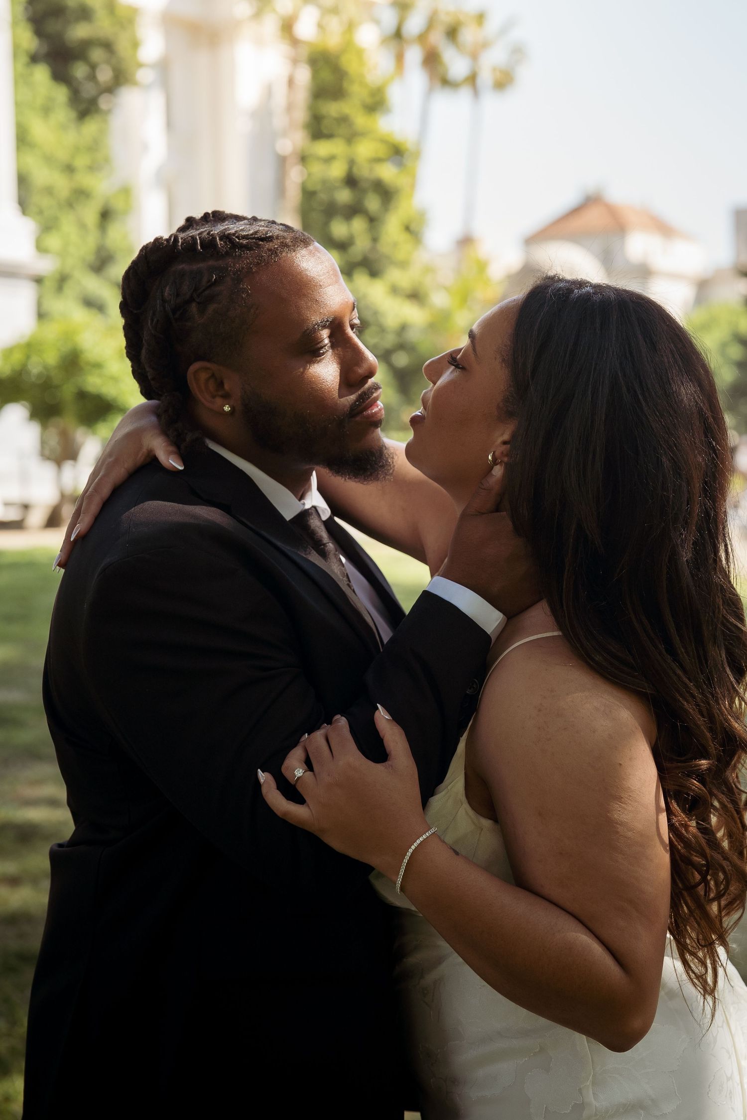 Couple in wedding attire share a romantic moment outdoors, bride in white dress and groom in black suit.