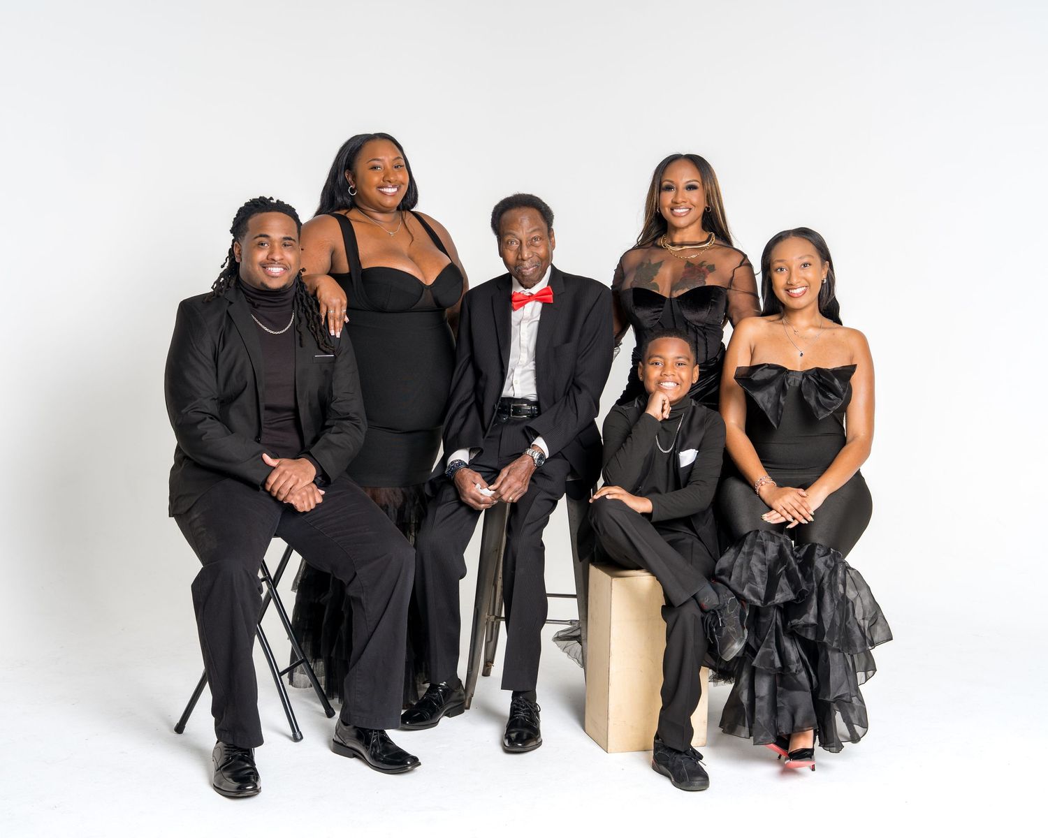 A family of six dressed in coordinating black formal attire pose for a professional studio portrait.