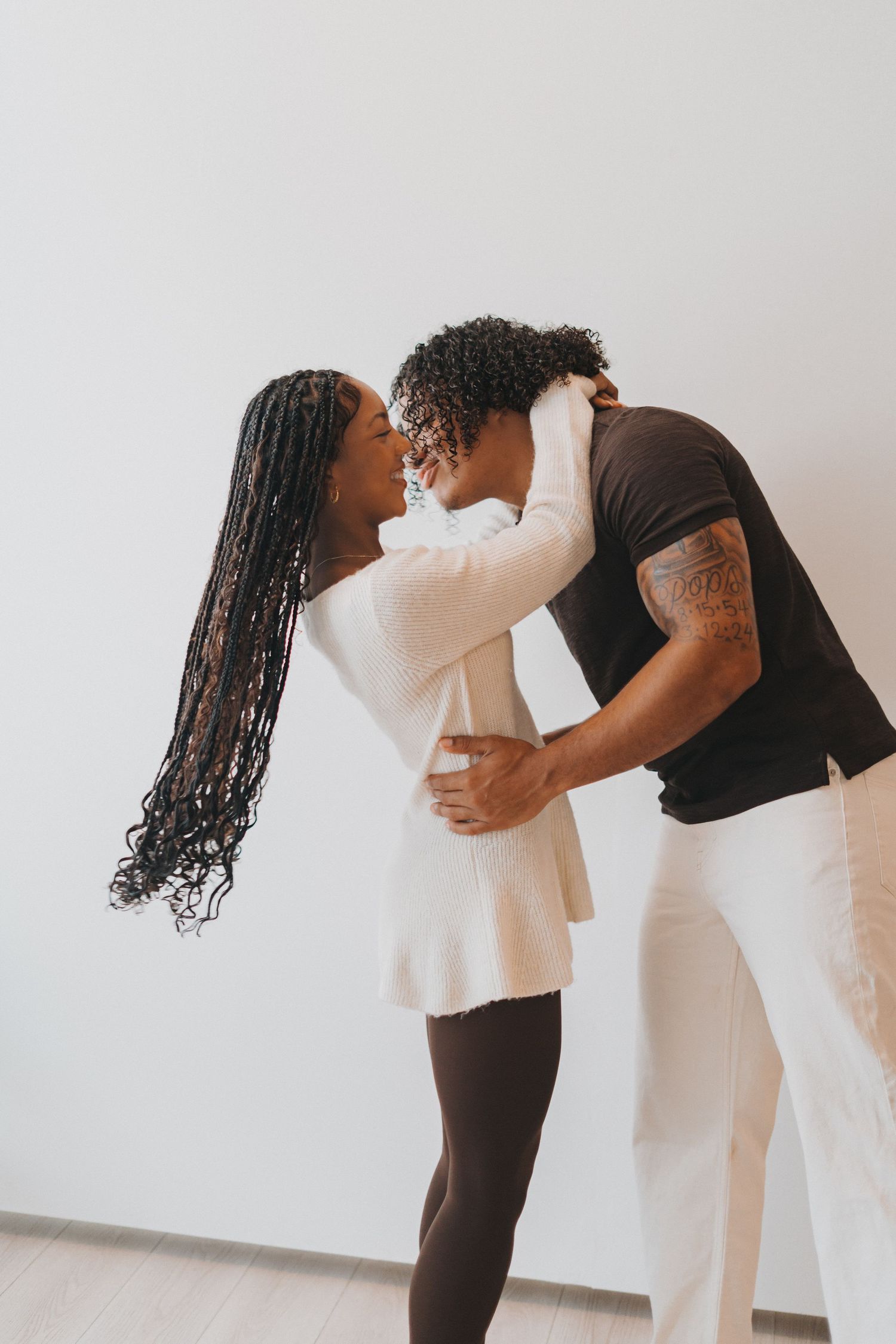 Affectionate couple shares romantic moment embracing and kissing in white studio space.