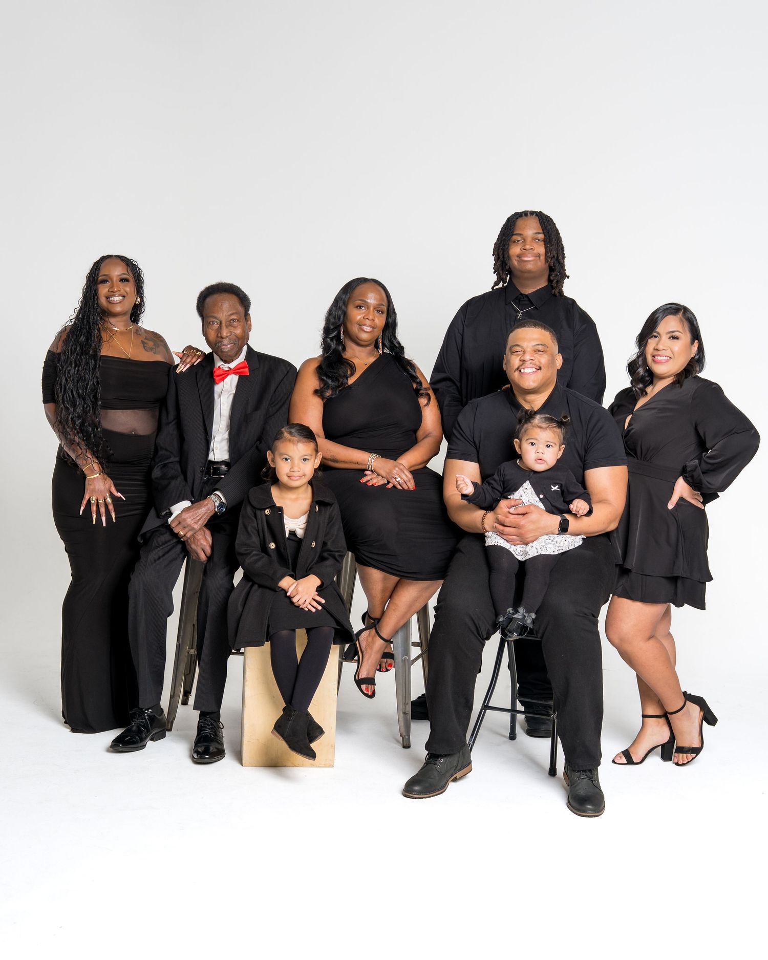 Large family group of eight poses in black outfits with two young children included.