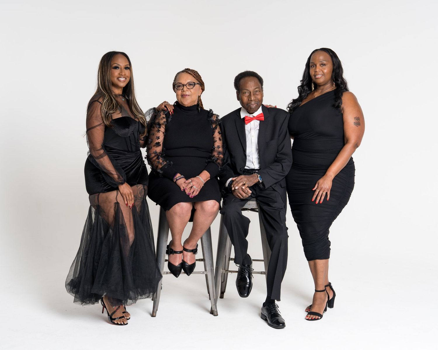 Four adults in elegant black formal wear pose together for professional family portrait.
