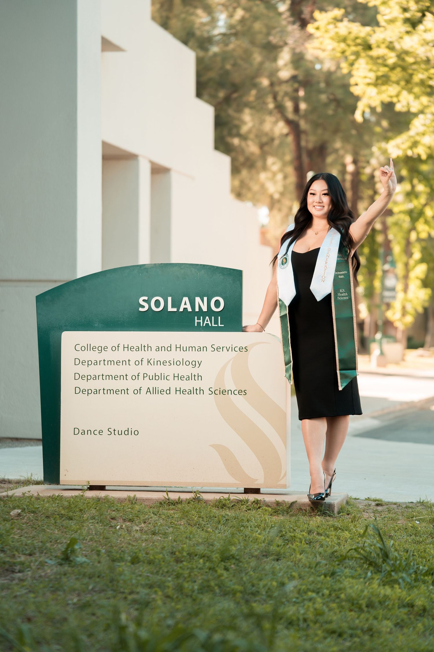 Smiling graduate poses beside Solano Hall sign at California State University campus.