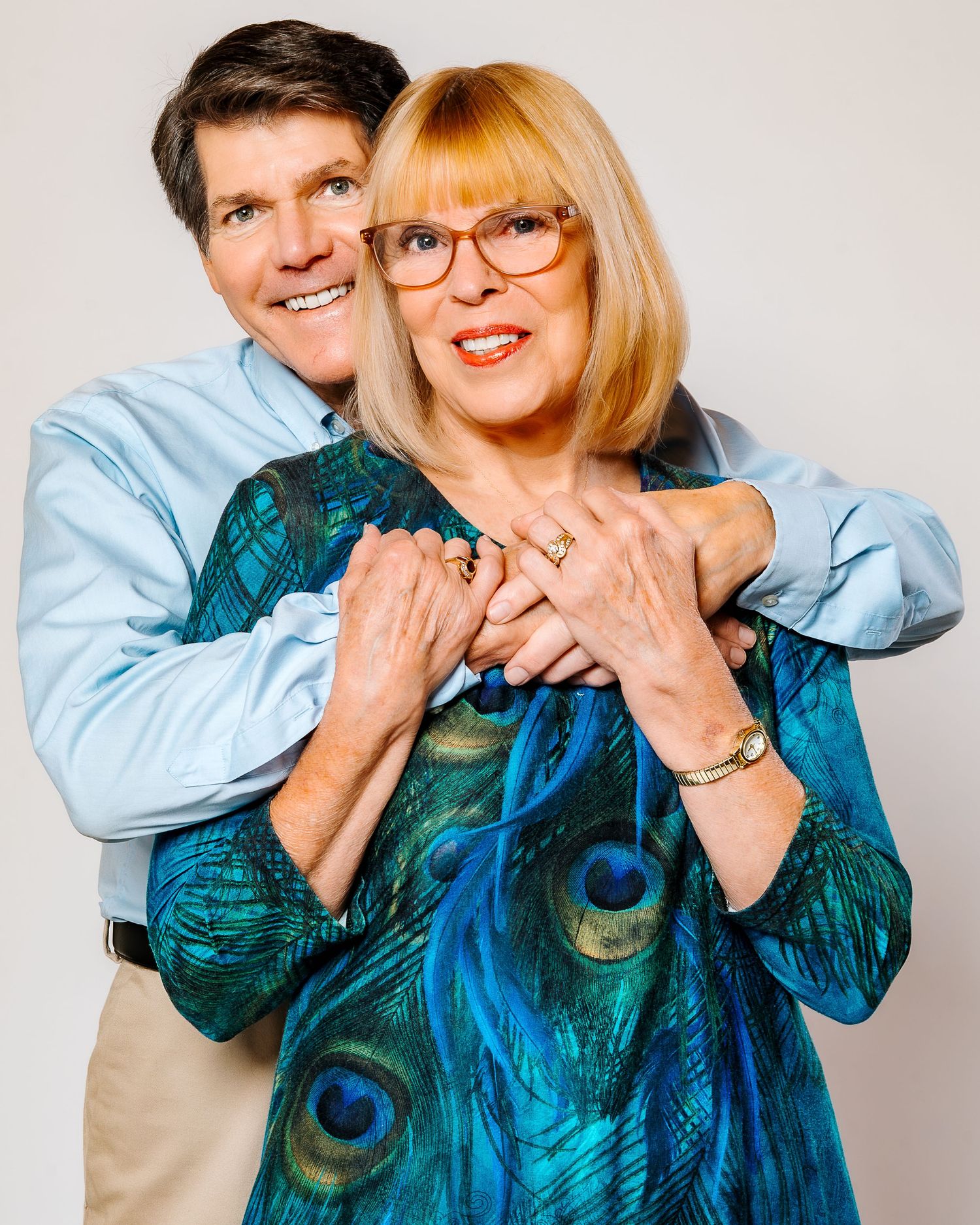 Happy couple embracing in a studio portrait, woman wearing a teal peacock-print blouse.