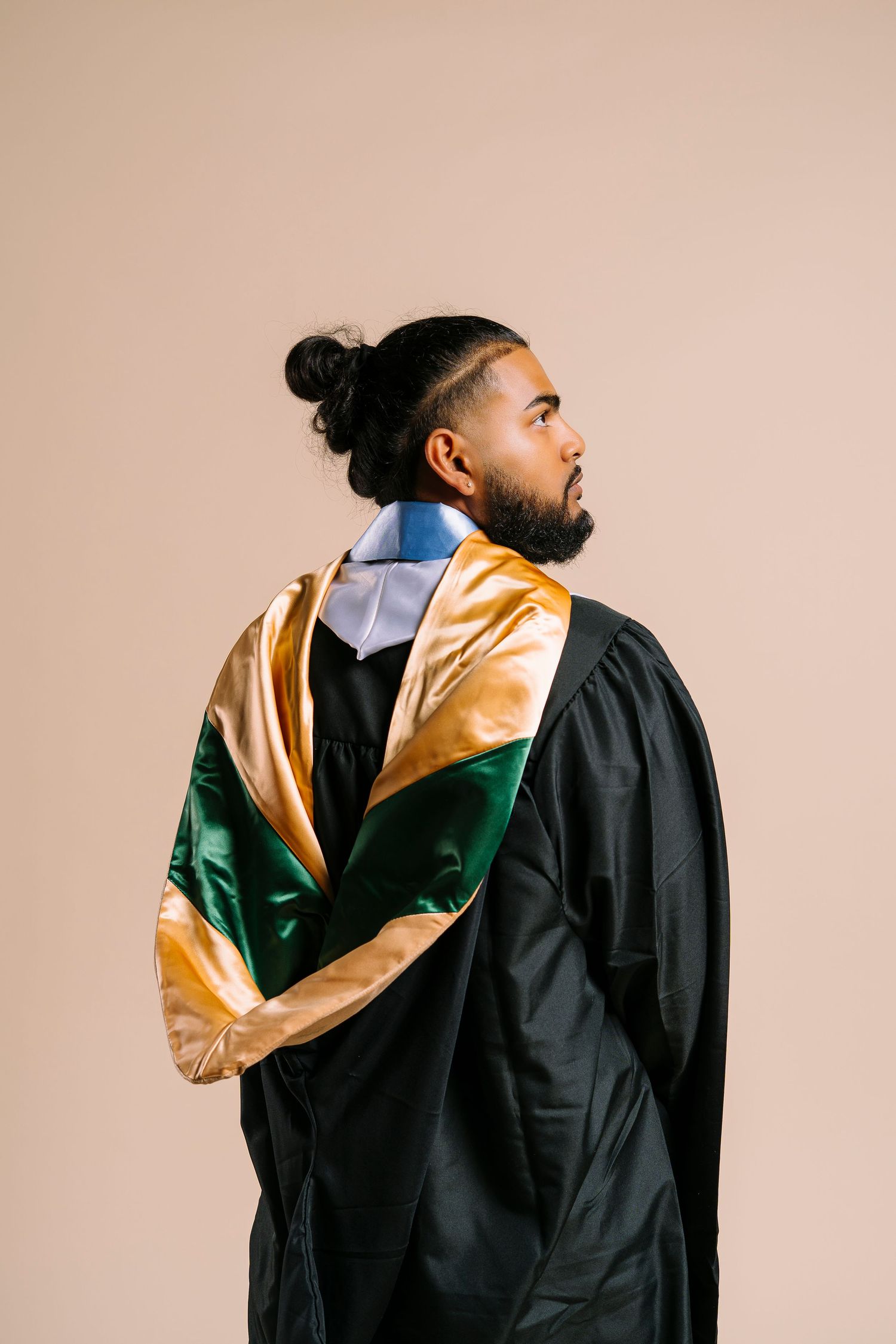 Graduate in black gown with green and gold hood viewed from behind.